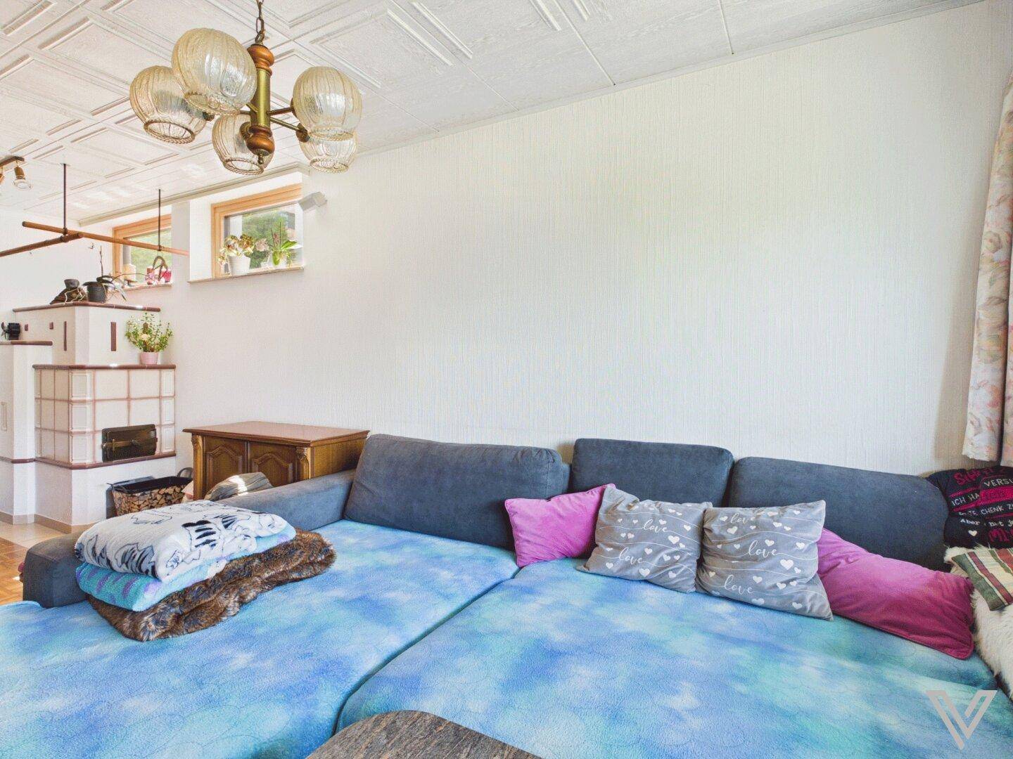 Geräumiges Wohnzimmer mit großer Eckcouch, Kachelofen und traditioneller Deckenverkleidung.