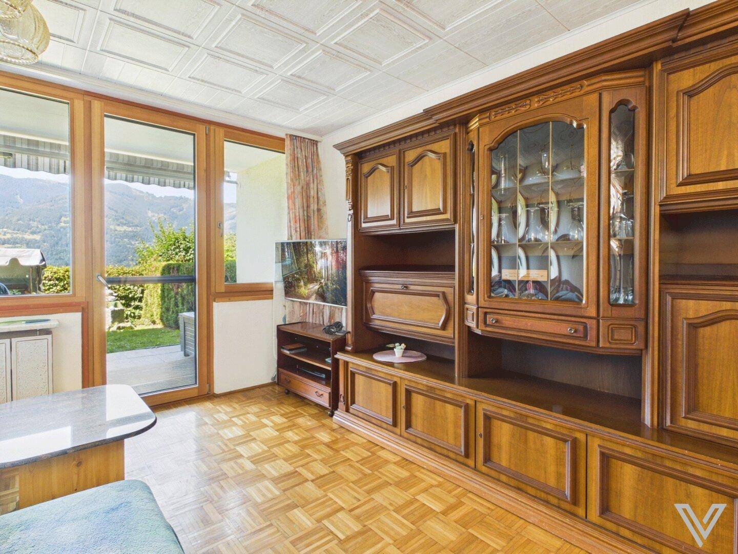 Gemütliches Wohnzimmer mit Holzboden, großer Schrankwand und Zugang zur Terrasse mit Bergblick.