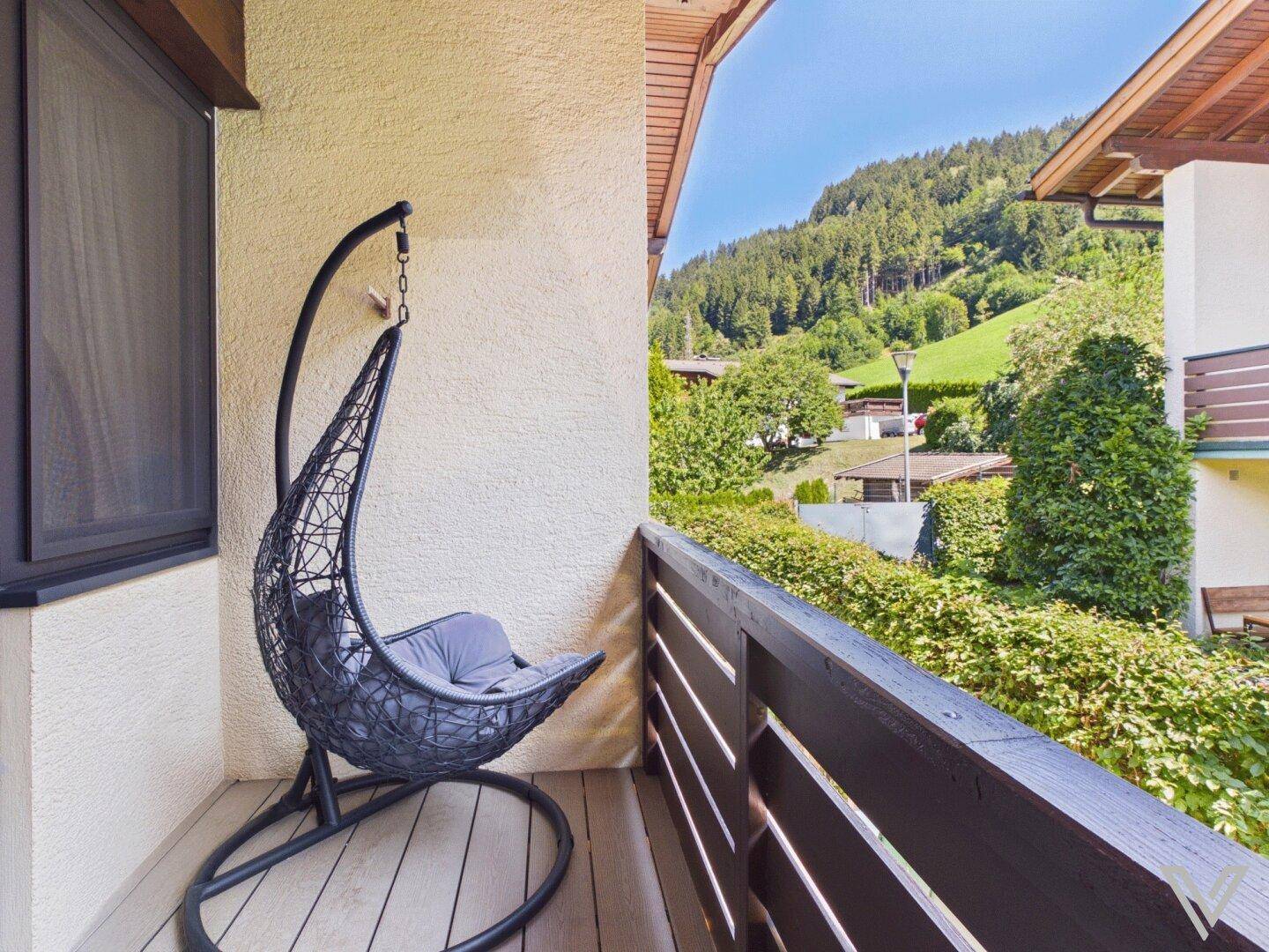 Gemütlicher Balkon mit Hängesessel und Blick auf die grüne Berglandschaft.