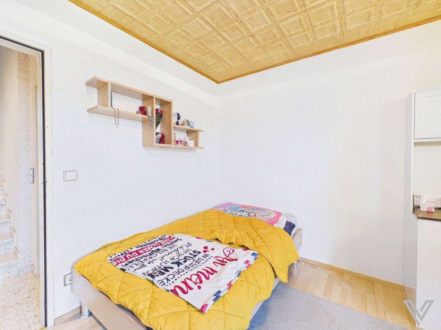 Kleines Schlafzimmer mit Einzelbett, Holzdecke und Regal an der Wand.