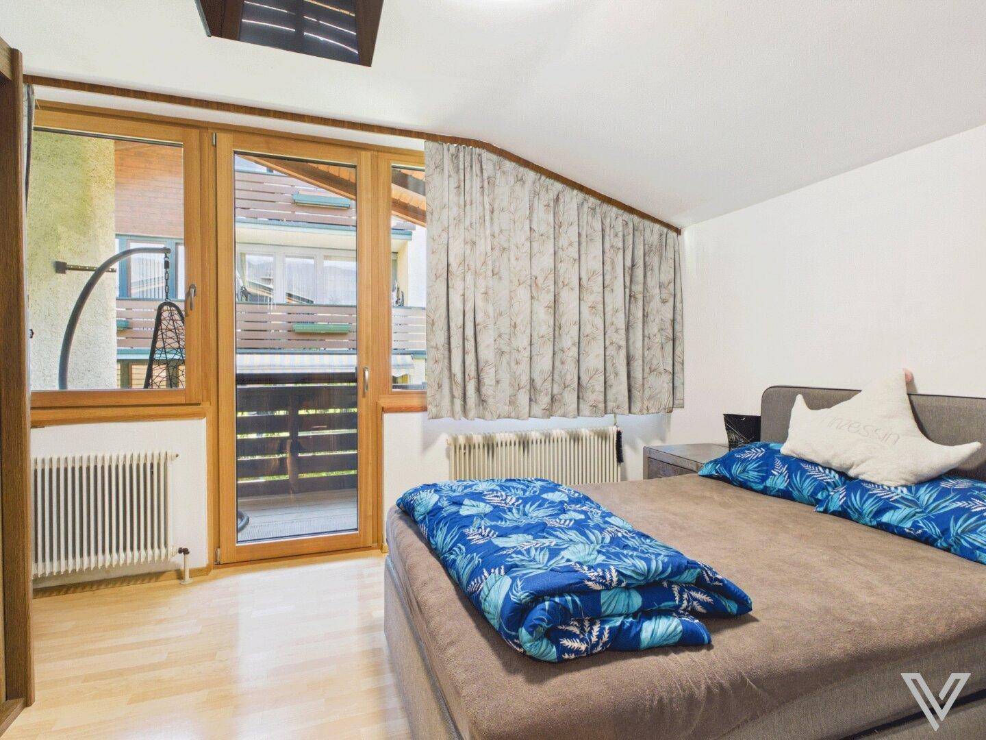 Helles Schlafzimmer mit Holzboden, Zugang zum Balkon und Blick auf die Umgebung.