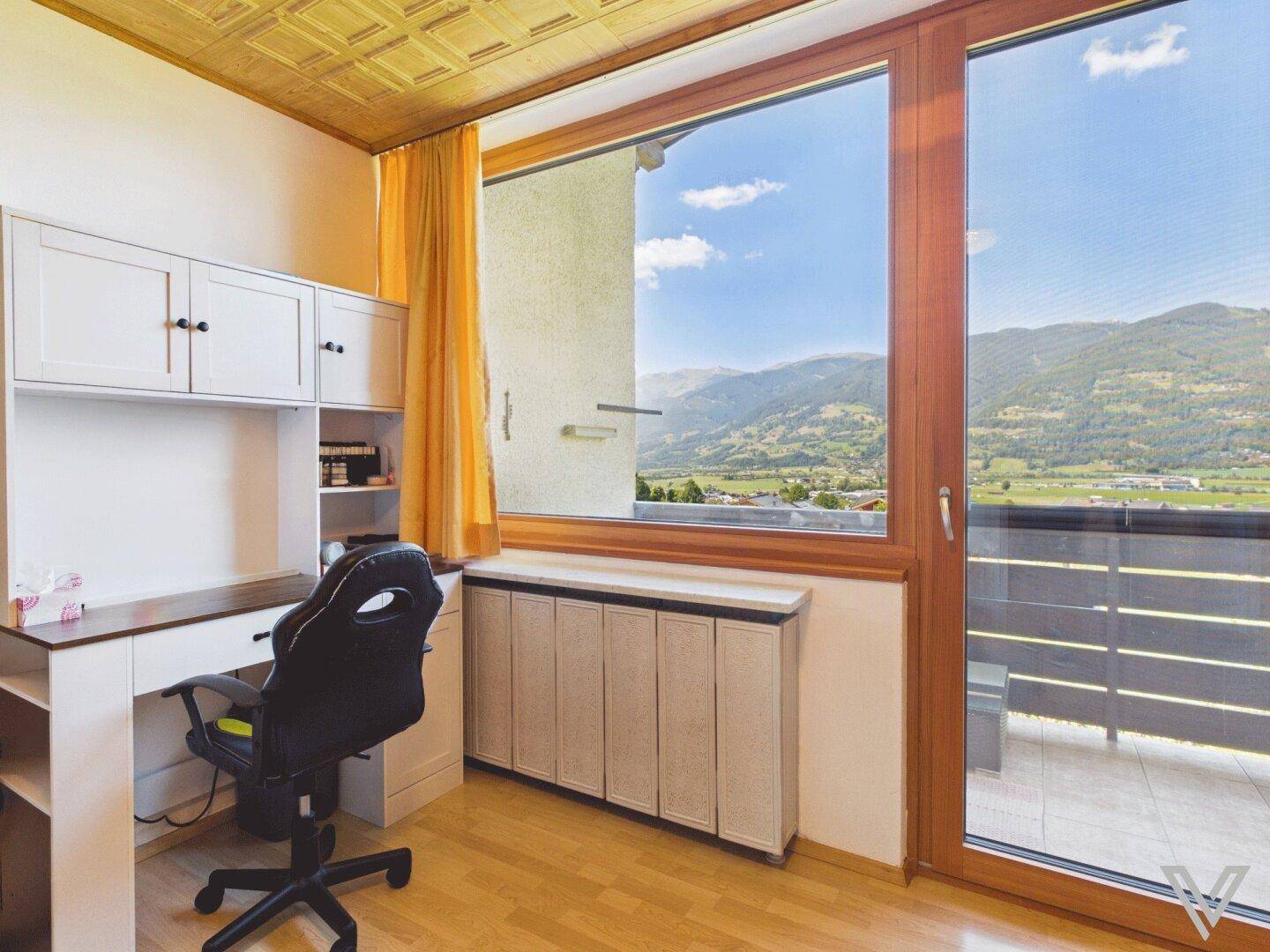 Helles Arbeitszimmer mit Schreibtisch, Bürostuhl und großem Fenster mit Bergblick.