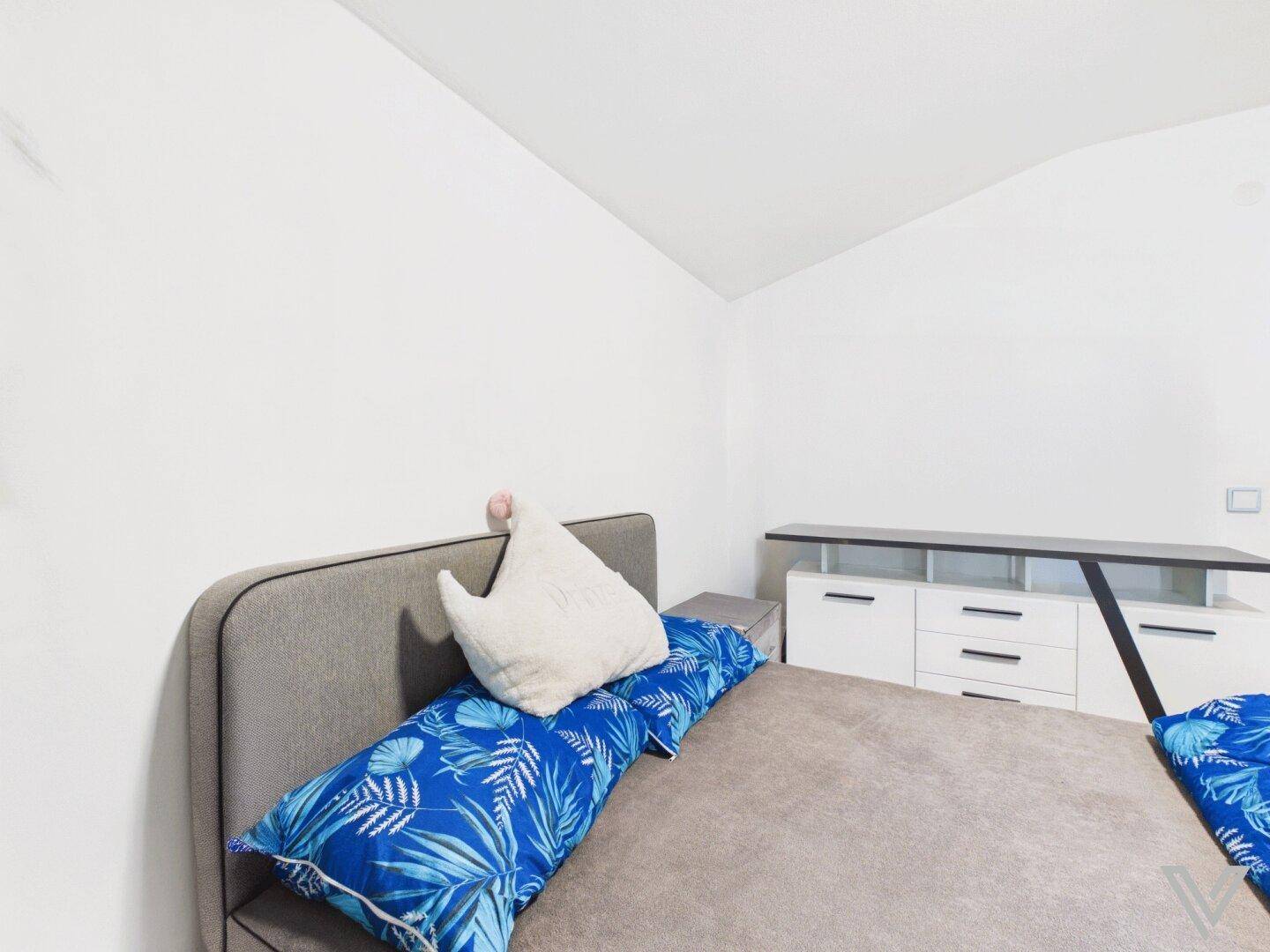 Schlafzimmer mit schrägen Wänden, Doppelbett und moderner Kommode.