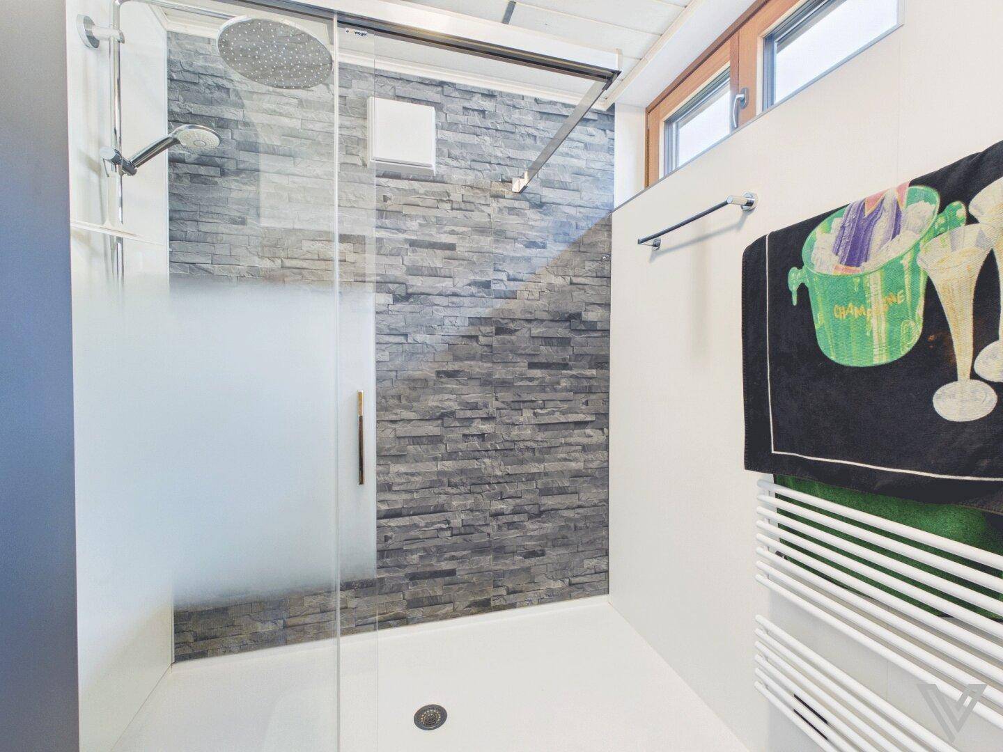 Geräumige Duschkabine mit Regendusche, Steinwand und Fenster für Tageslicht.