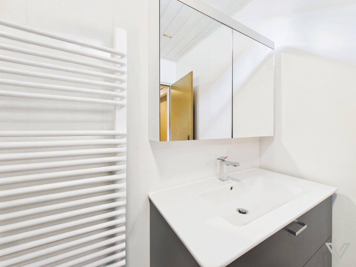 Modernes Badezimmer mit Einzelwaschbecken, Spiegelschrank und beheiztem Handtuchhalter.