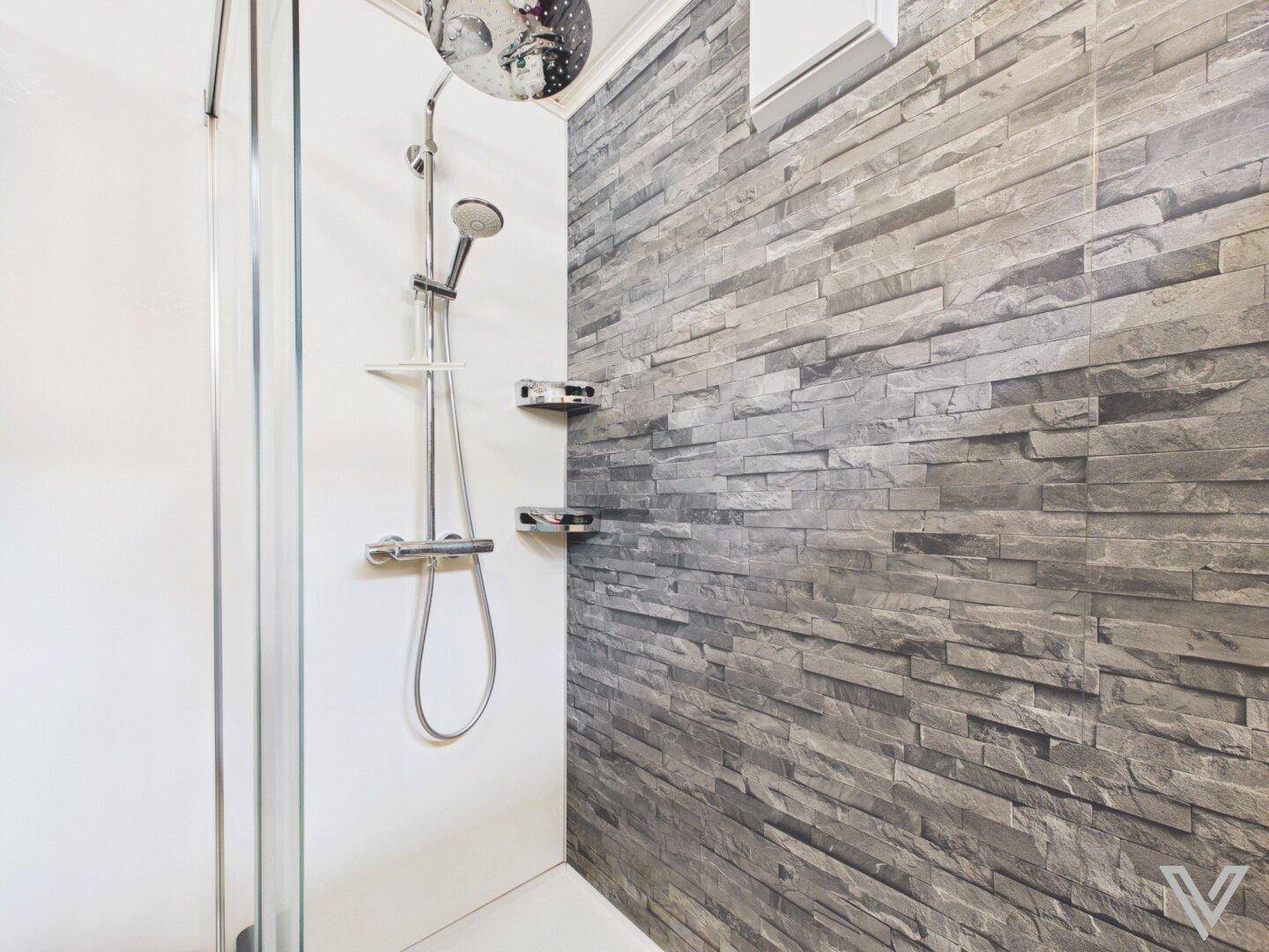 Duschbereich mit Steinoptik-Fliesenwand und moderner Regendusche.
