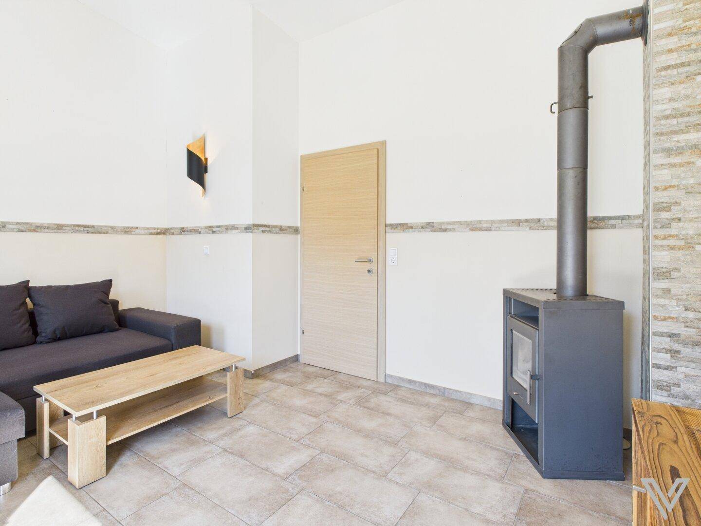 Wohnzimmer mit Kaminofen, bequemer Couch und Zugang zu weiteren Räumen.