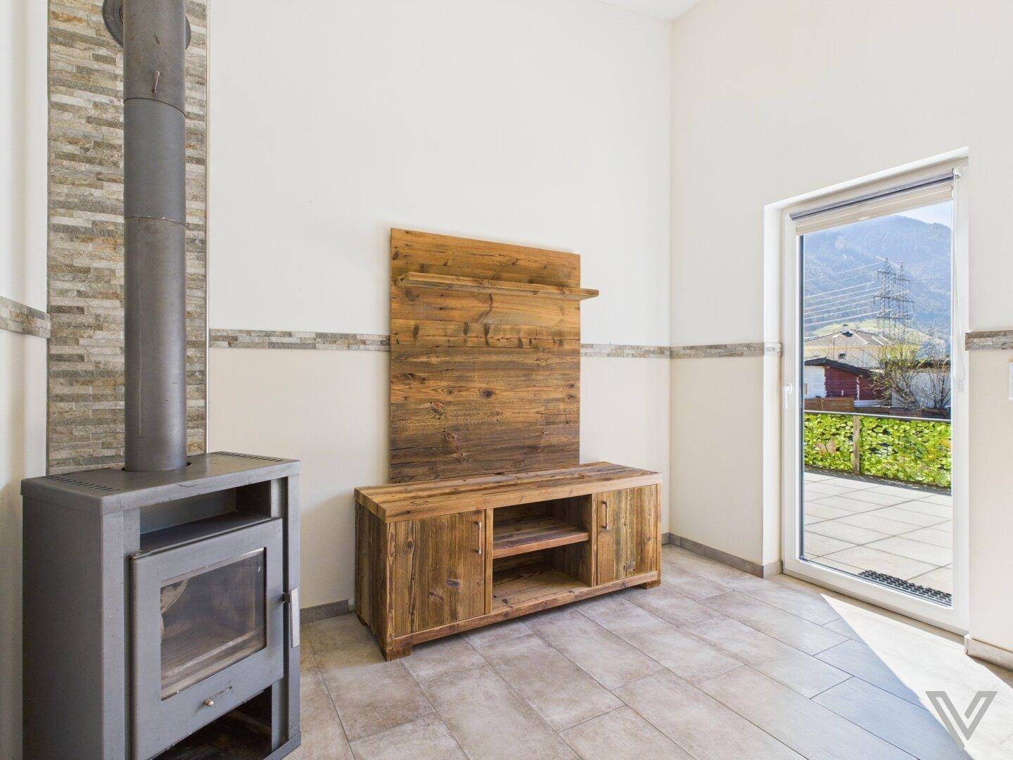 Gemütlicher Wohnbereich mit Kaminofen, Holzmöbeln und Blick auf die Berge durch die Terrassentür.