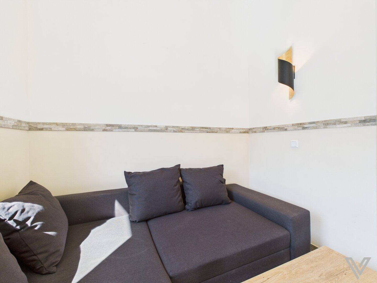 Detailansicht einer modernen Wandleuchte über einer dunklen Couch im Wohnzimmer.