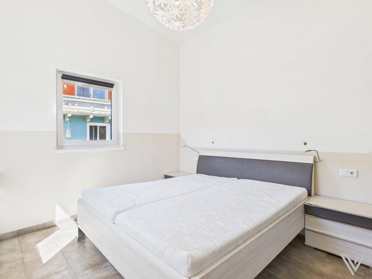 Helles Schlafzimmer mit Doppelbett, Nachttischen und Blick auf die Nachbarhäuser.