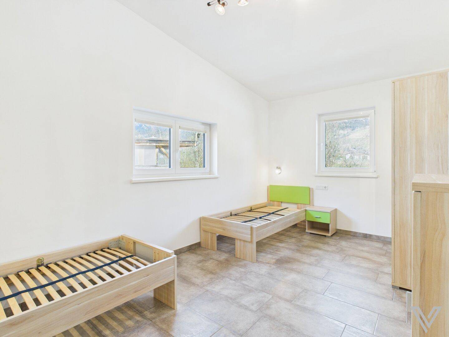 Helles Kinderzimmer mit zwei Einzelbetten und Fenstern mit Blick ins Grüne.