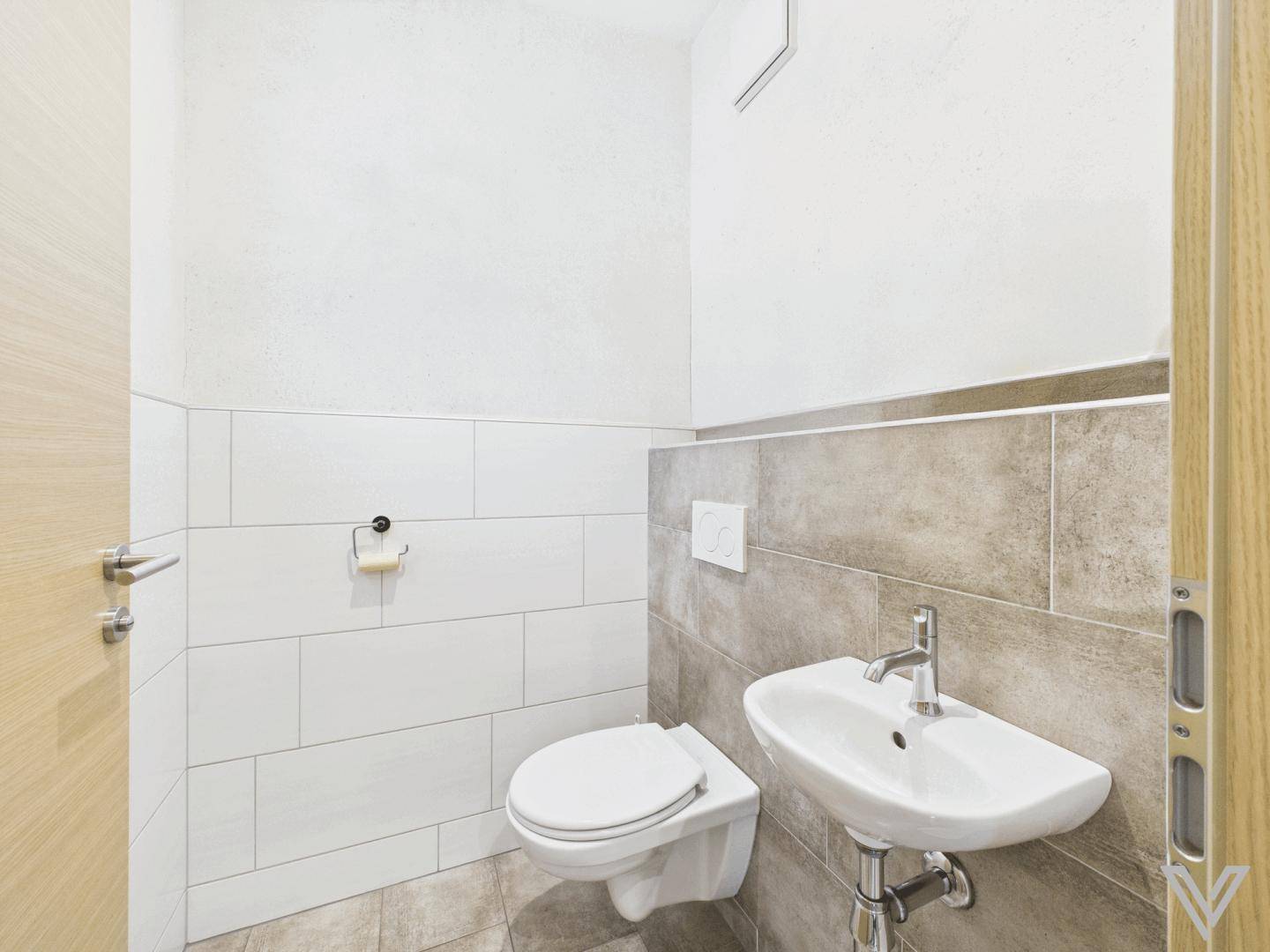 Separates WC mit Wand-WC und kleinem Handwaschbecken, modern gefliest.
