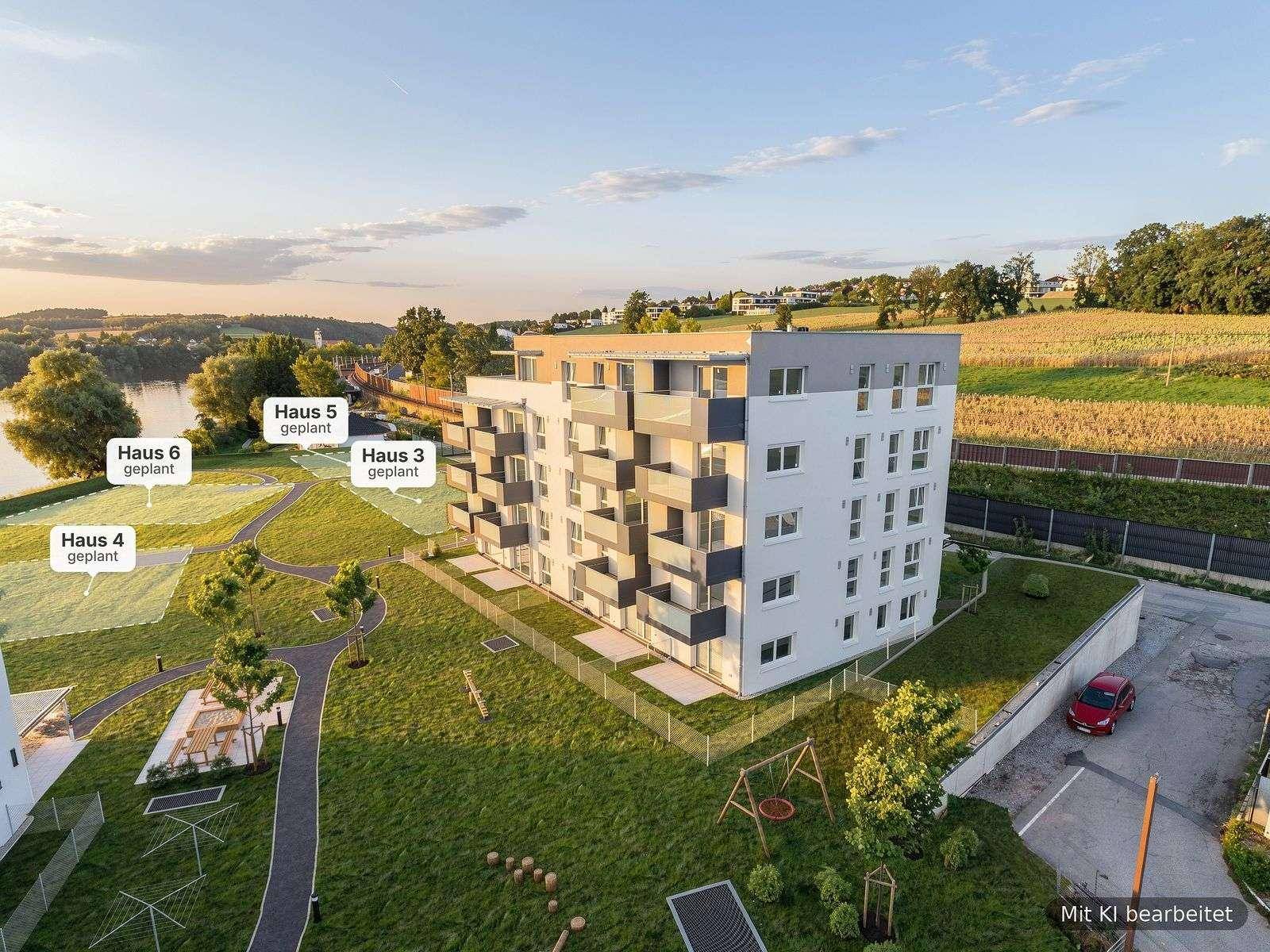 Luftaufnahme eines modernen Wohnkomplexes mit grünen Außenanlagen und Blick auf einen Fluss.