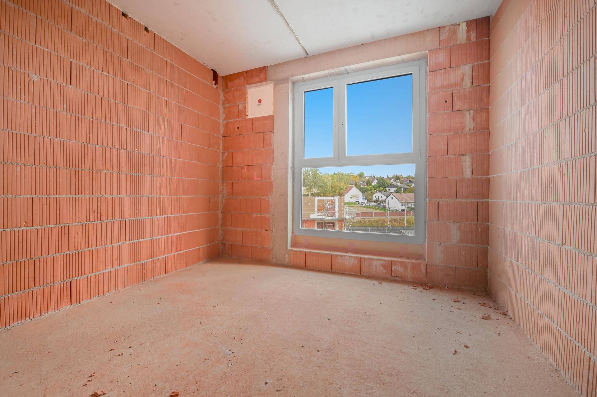 Unverputzter Raum mit Ziegelwänden und einem Fenster, das einen Blick auf die Nachbarschaft freigibt.