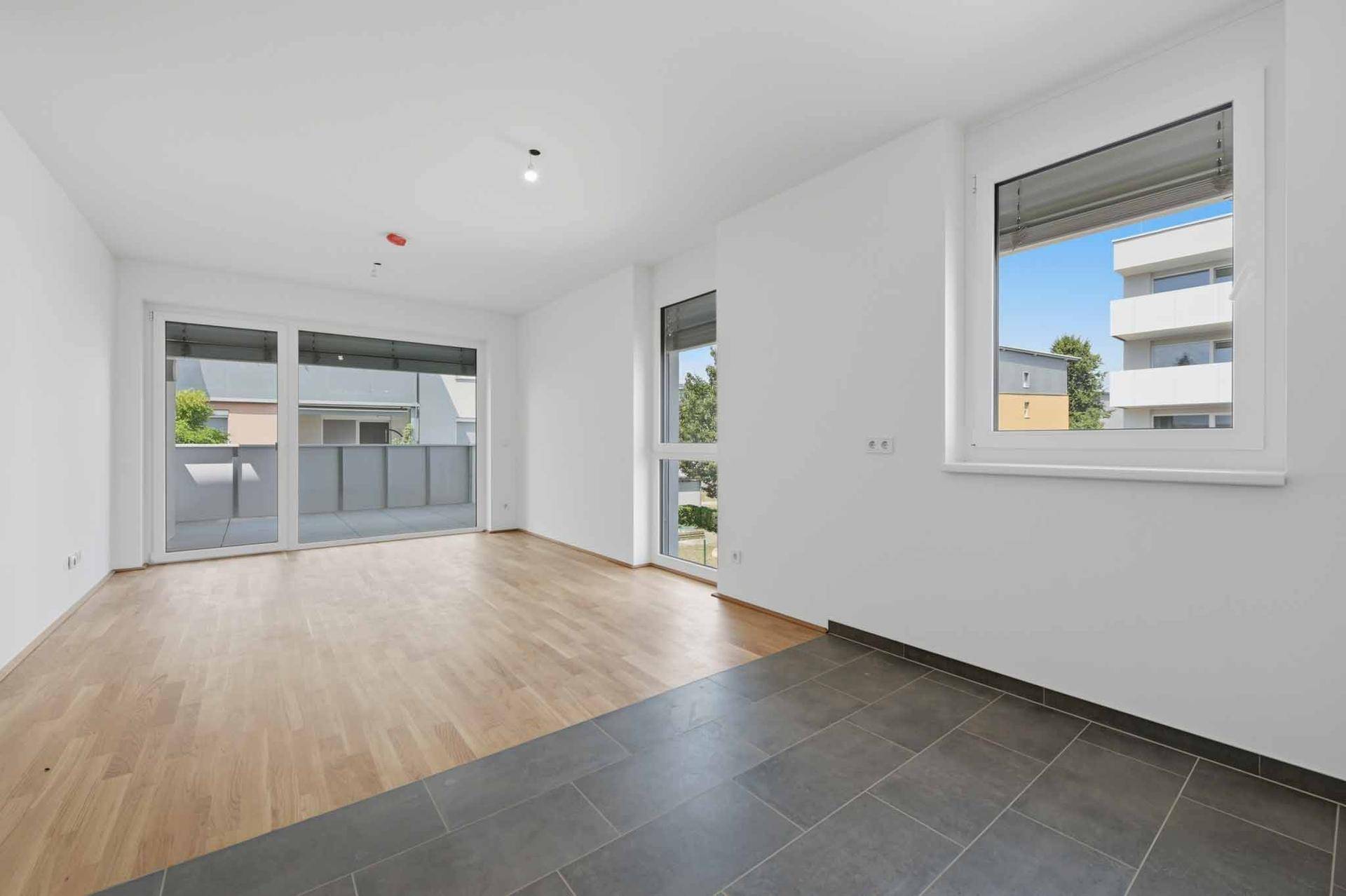 Geräumiger, heller Wohnbereich mit Holzboden und Fliesen, Zugang zu einem Balkon.