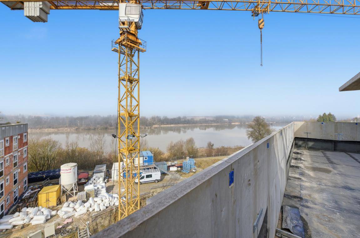 Panoramablick über einen Fluss mit einem großen Baukran im Vordergrund und Baustelle.