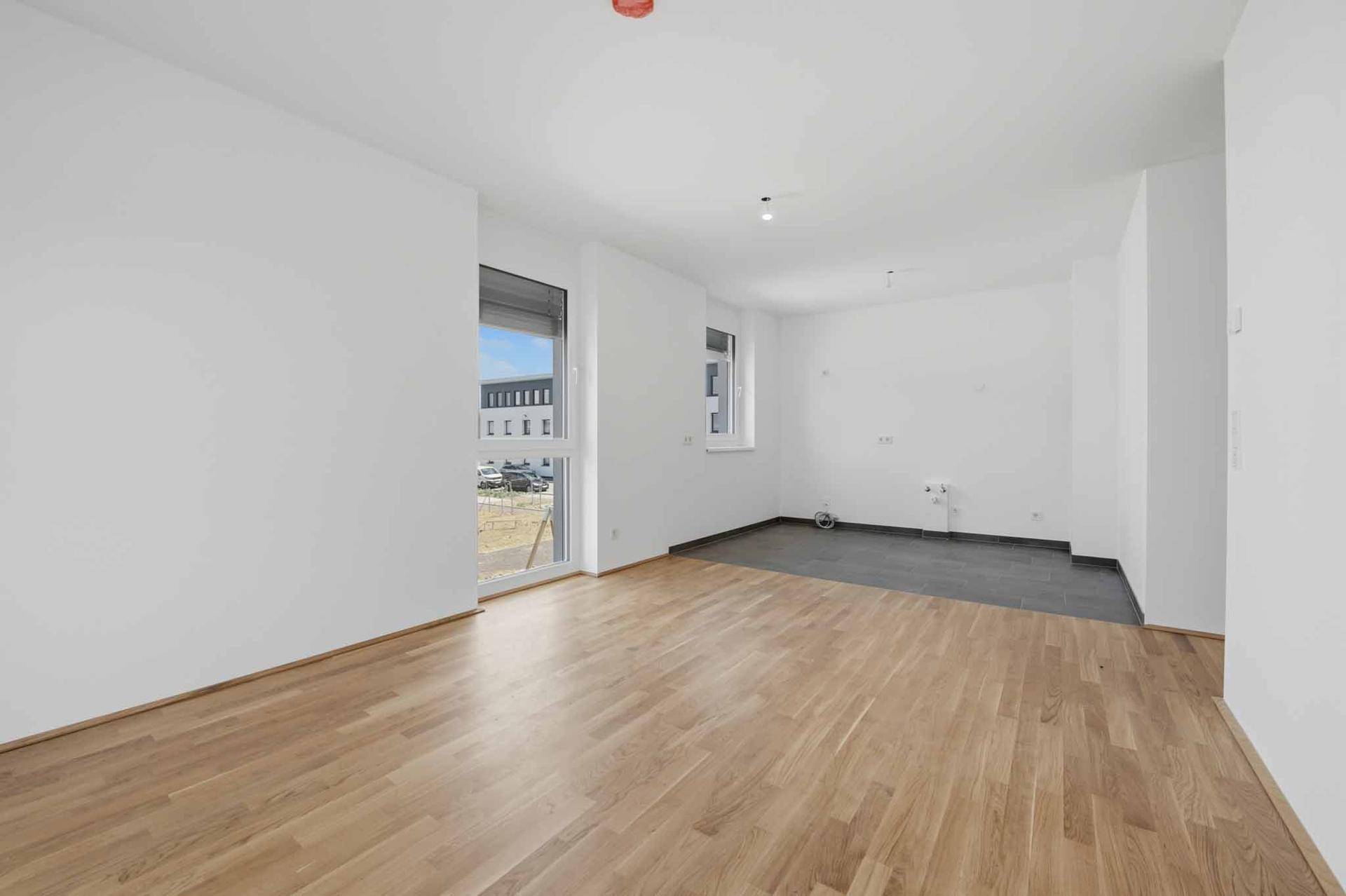 Heller, leerer Raum mit Holzboden und einem gefliesten Bereich, ideal für eine offene Küche.