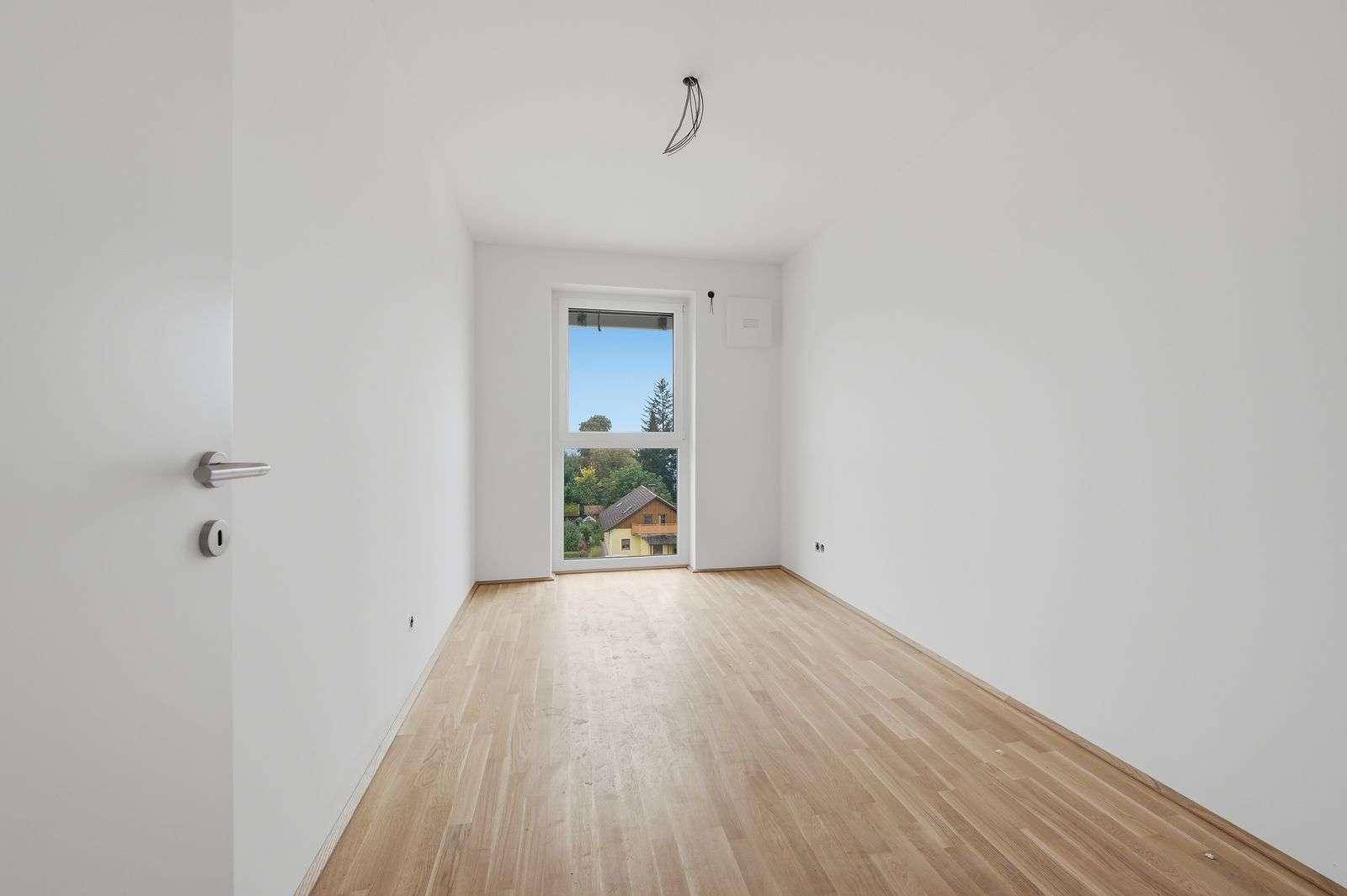 Unmöblierter Raum mit hellem Holzboden und großem Fenster, geeignet als Schlaf- oder Arbeitszimmer.