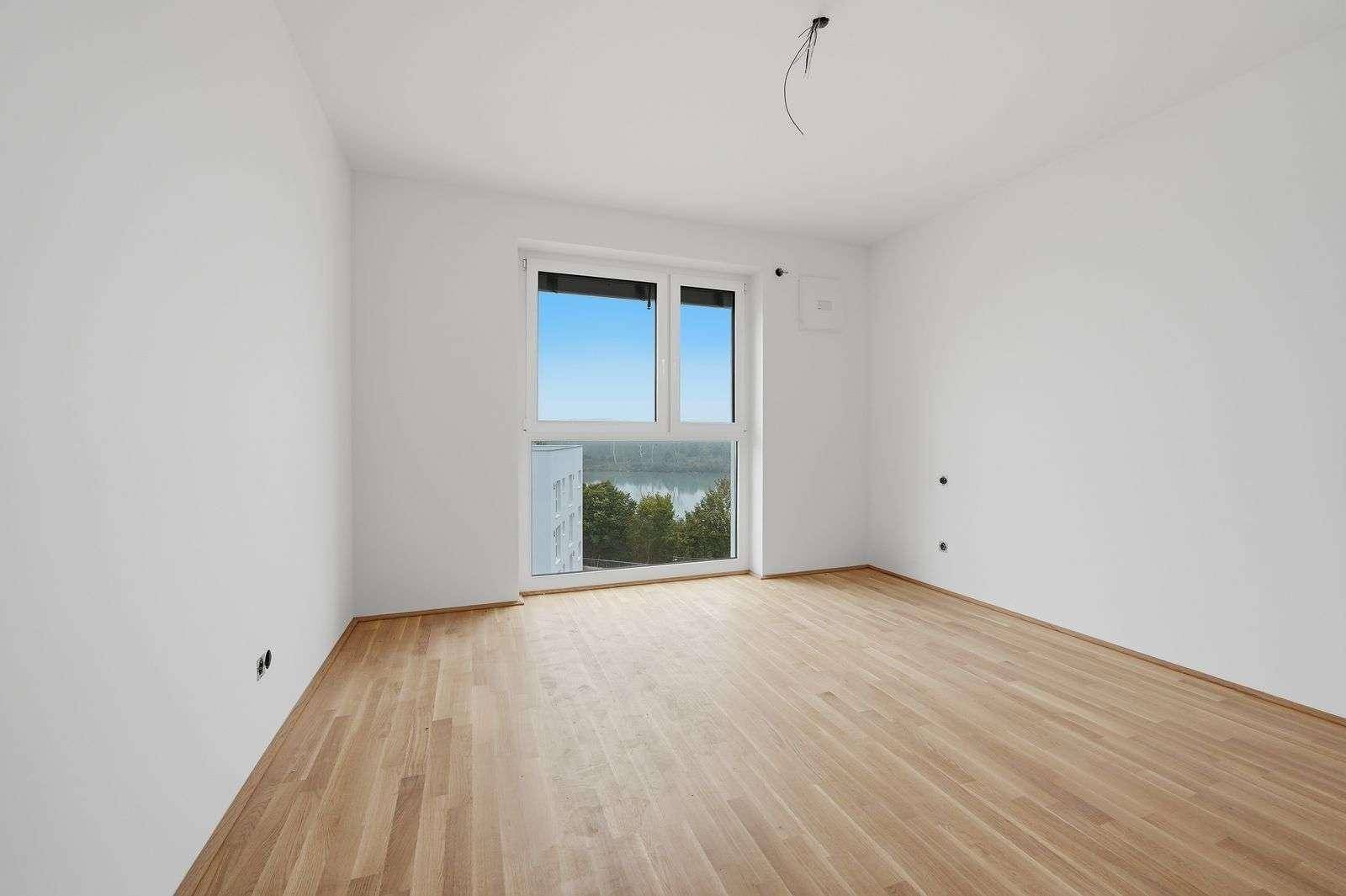 Unmöbliertes Schlafzimmer mit Holzboden und großem Fenster mit Blick auf das Wasser.