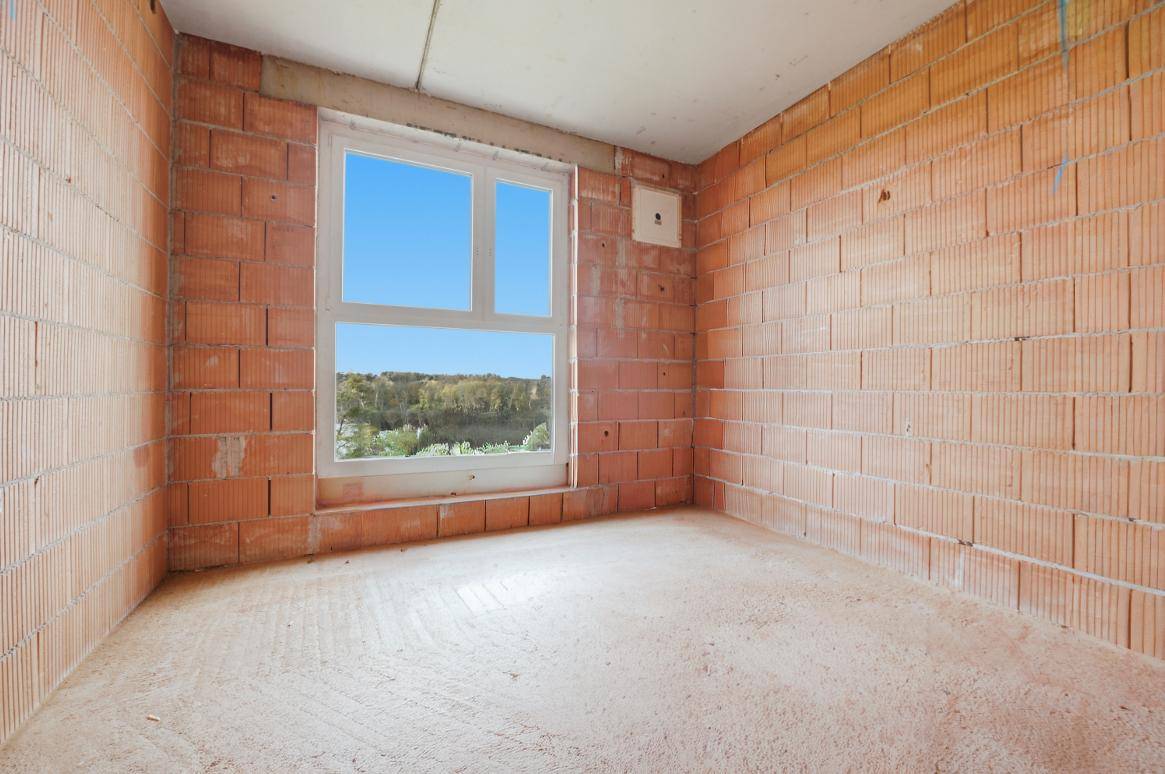 Unfertiger Innenraum mit Ziegelwänden und großem Fenster mit Blick ins Grüne.