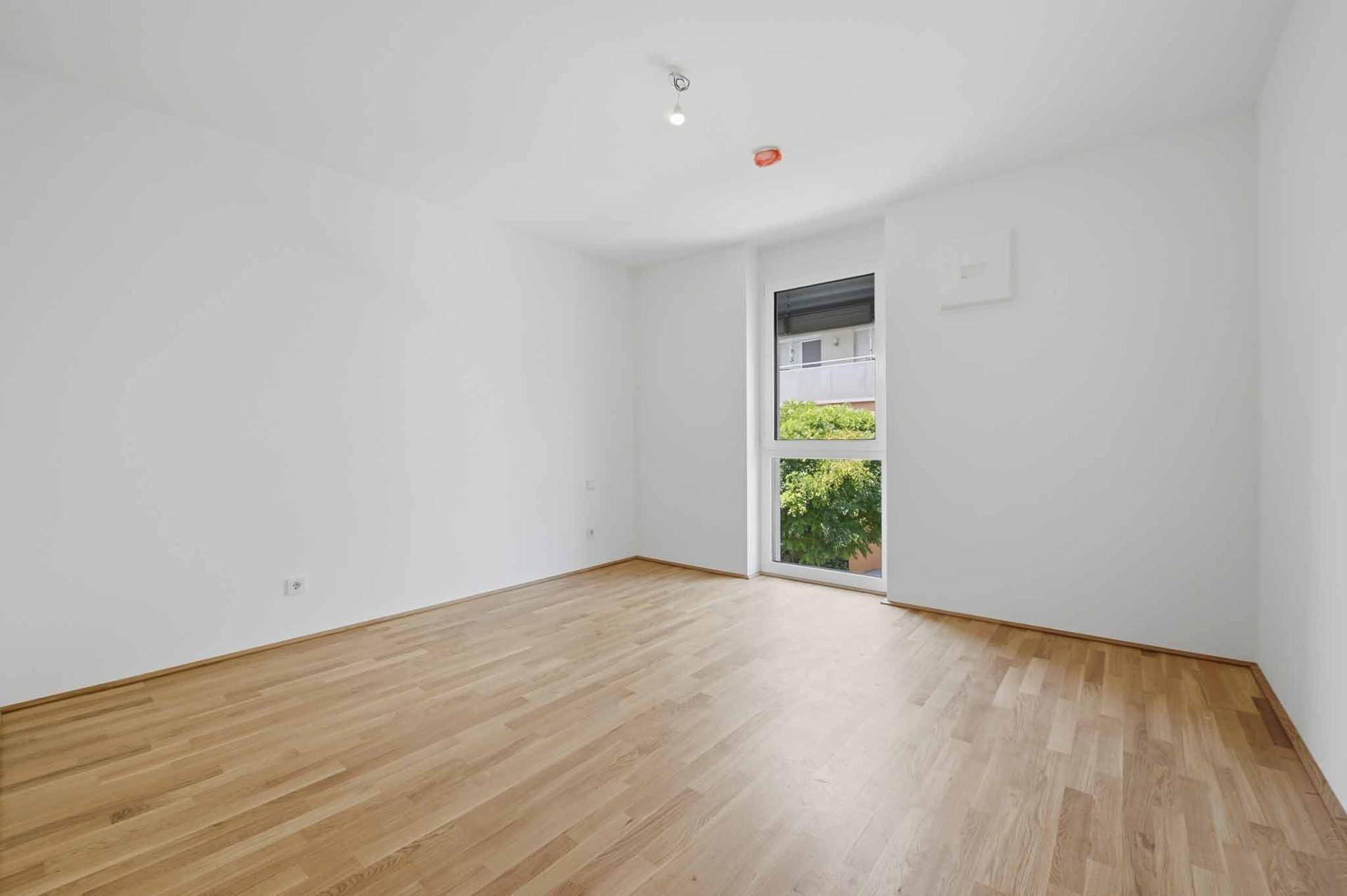 Helles Schlafzimmer mit Holzboden und großem Fenster, bietet eine ruhige Atmosphäre.