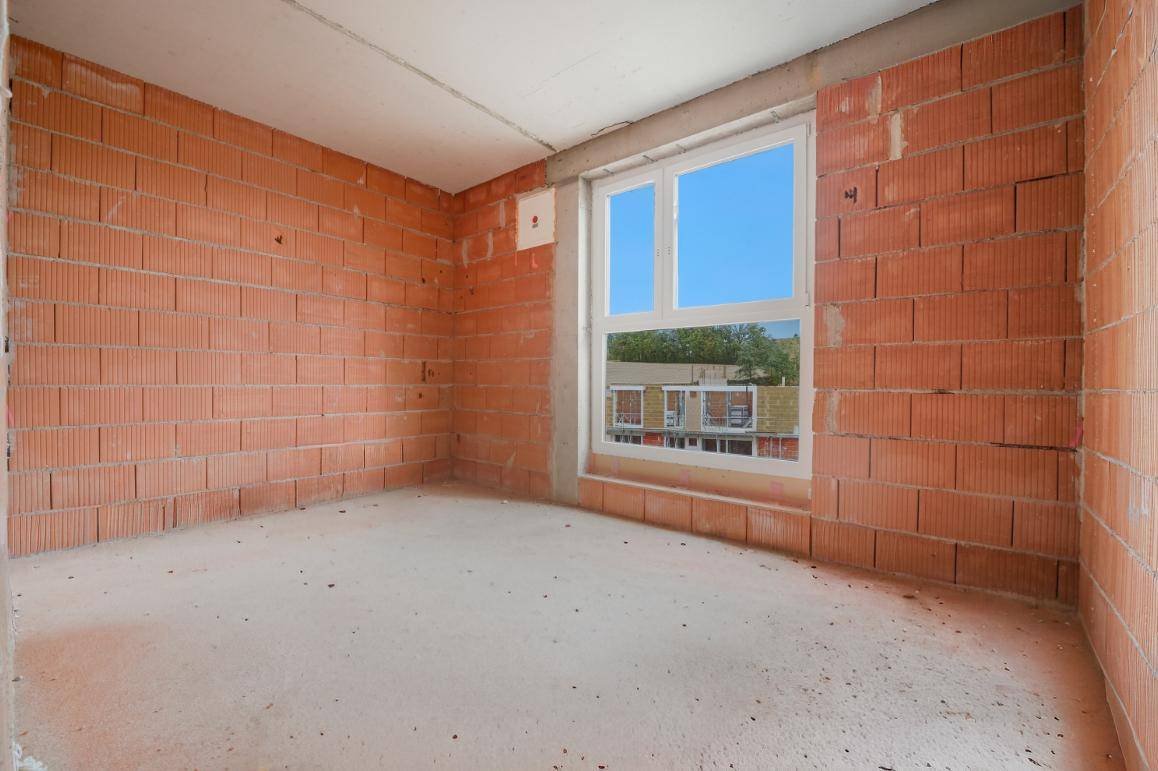 Unfertiger Innenraum mit unverputzten Ziegelwänden und einem Fenster mit Blick nach draußen.