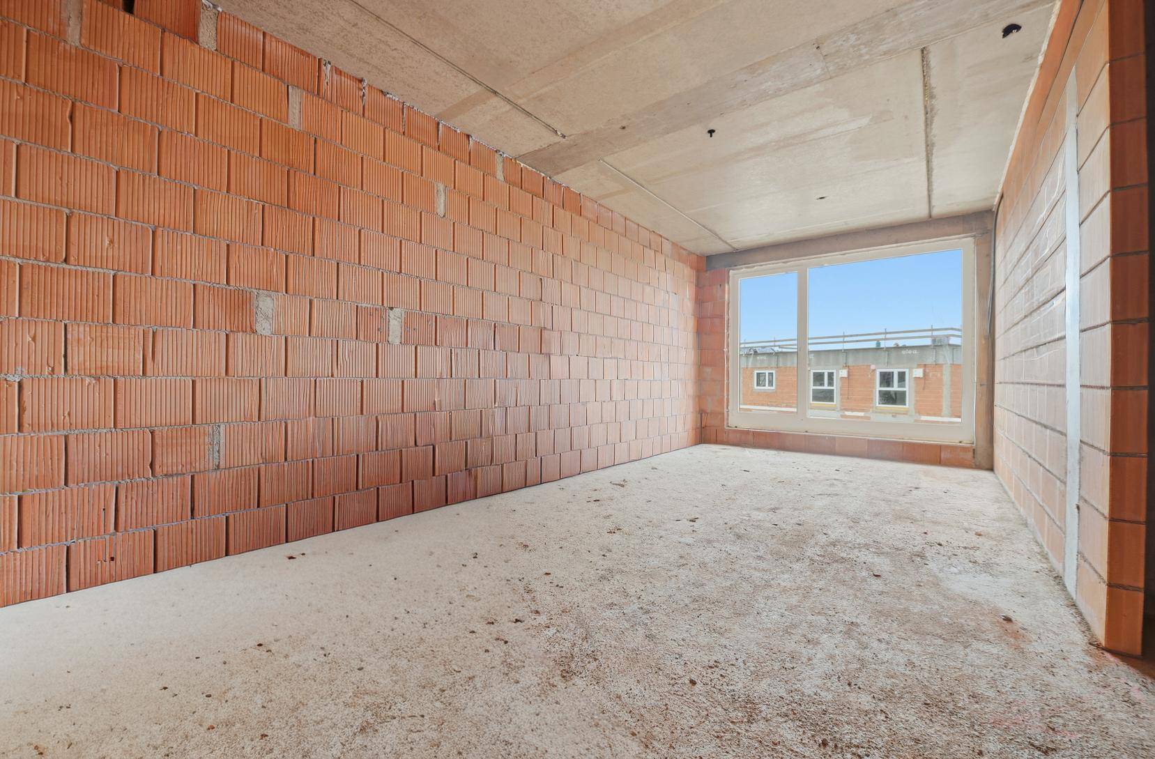 Rohbau-Zimmer mit unverputzten Ziegelwänden und Betonboden, bereit für den weiteren Ausbau.