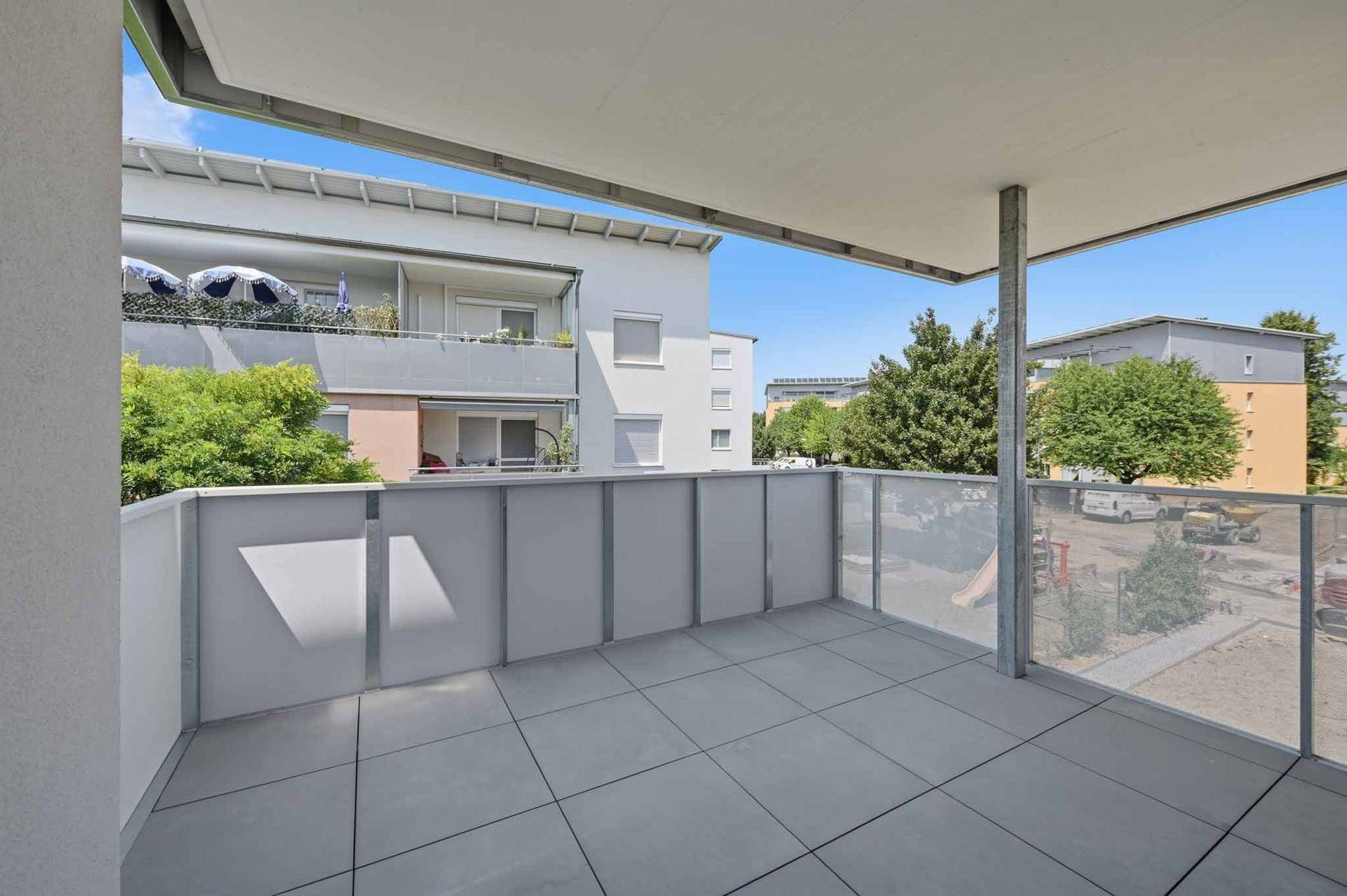 Heller Balkon mit Fliesenboden und Glasgeländer, bietet Blick auf die umliegende Wohngegend.
