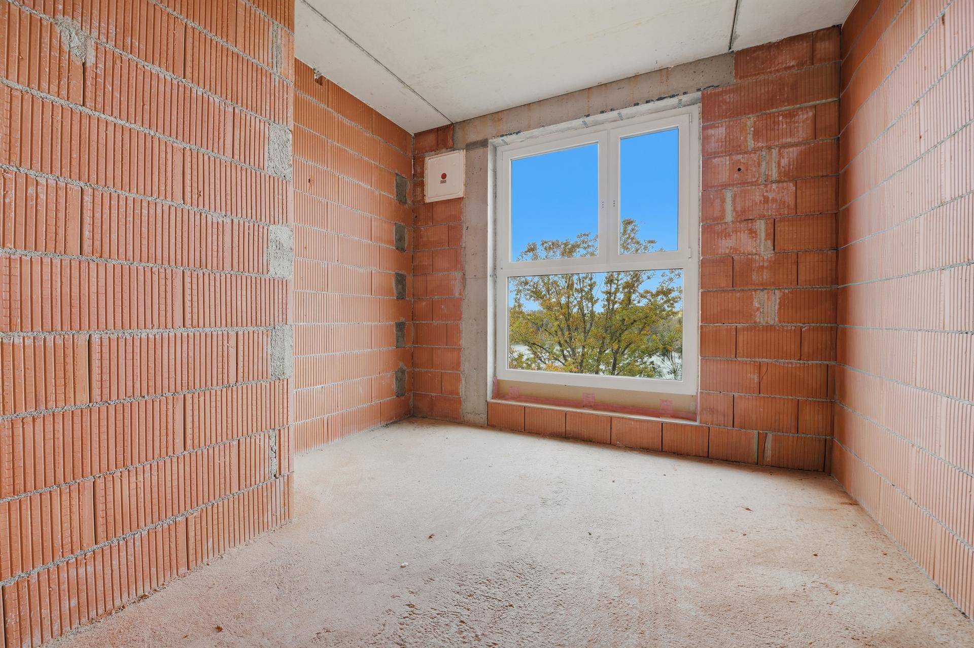 Rohbau-Innenraum mit Ziegelwänden und Fenster, das einen Blick auf Bäume bietet.