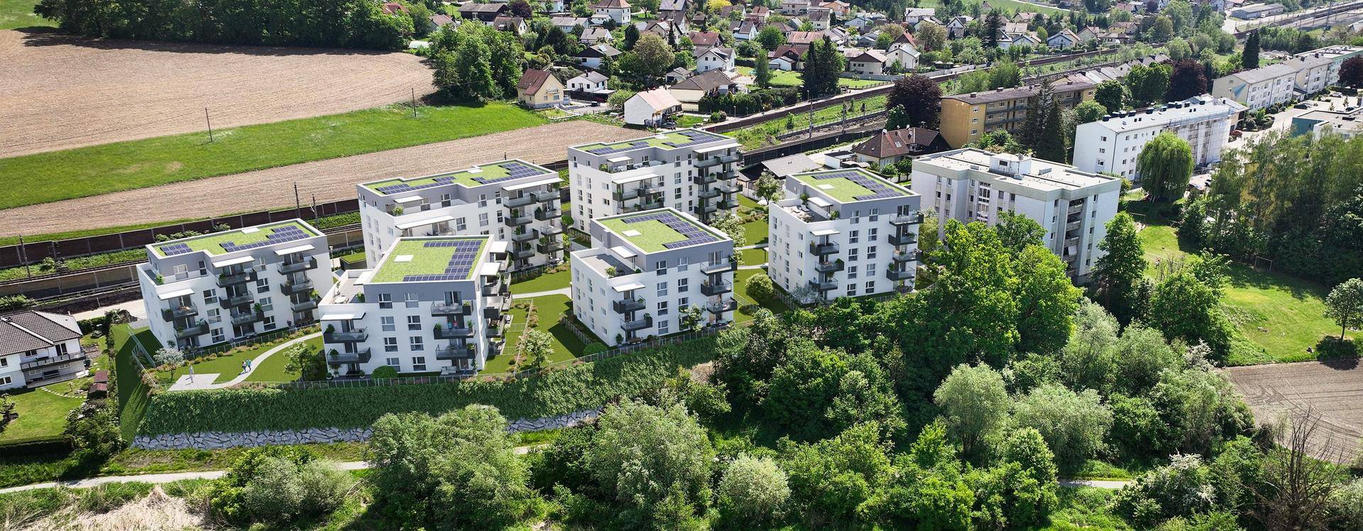 Luftaufnahme eines modernen Wohnkomplexes mit mehreren Gebäuden und Photovoltaikanlagen in grüner Umgebung.