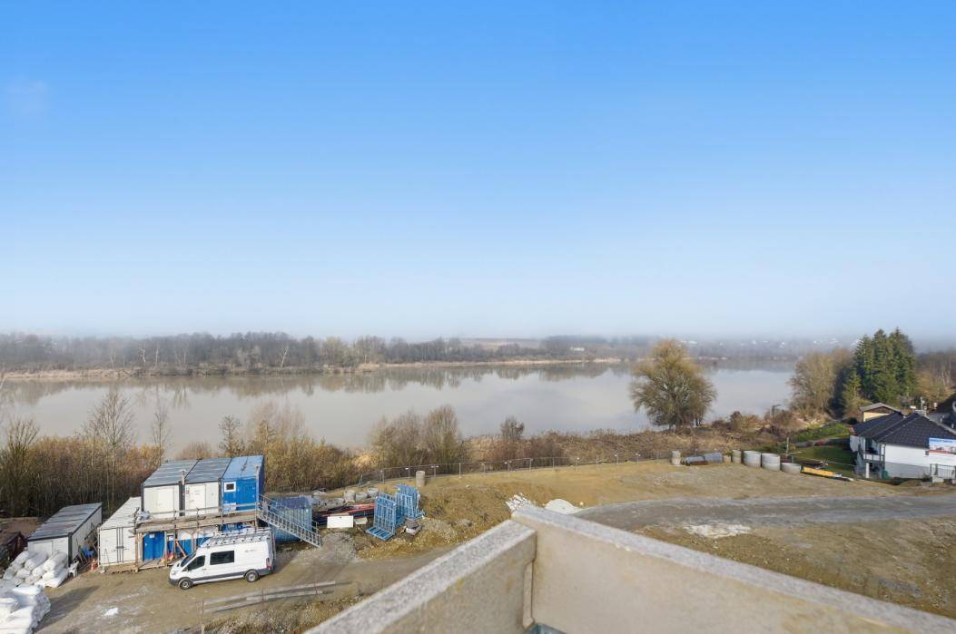 Weitblick über einen Fluss oder See mit umliegender Natur und Baustellenaktivitäten.