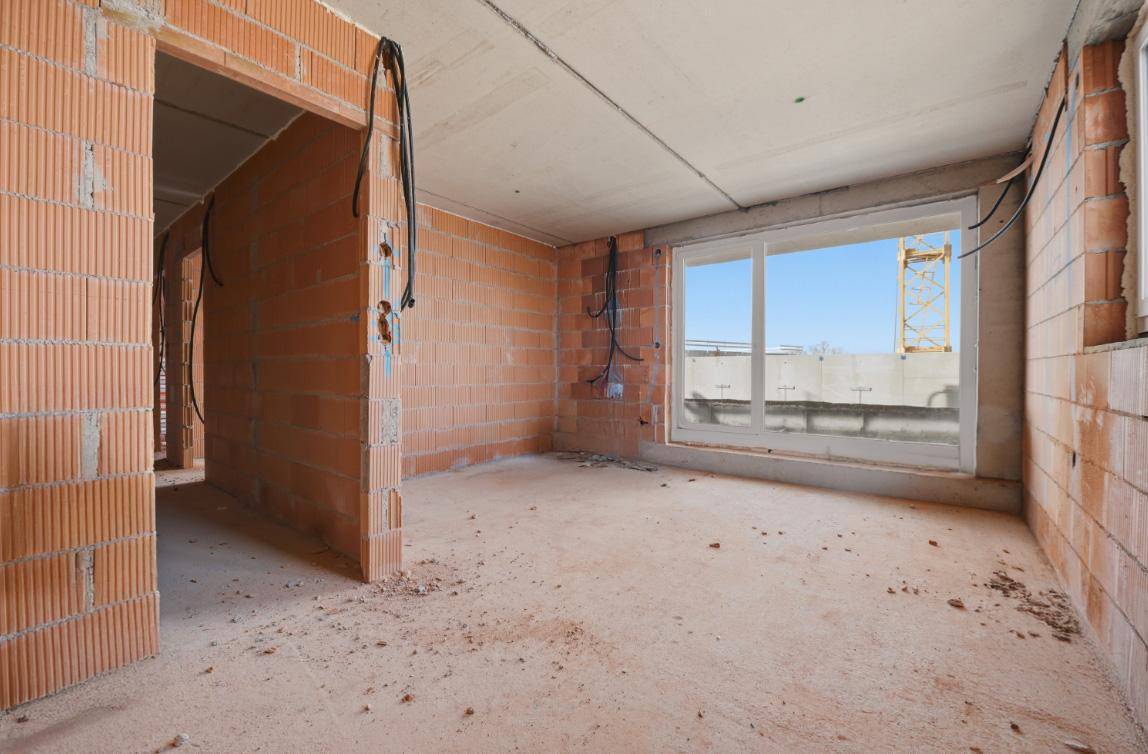 Unfertiger Innenraum im Rohbau mit Ziegelwänden, Betonboden und Blick auf die Baustelle.