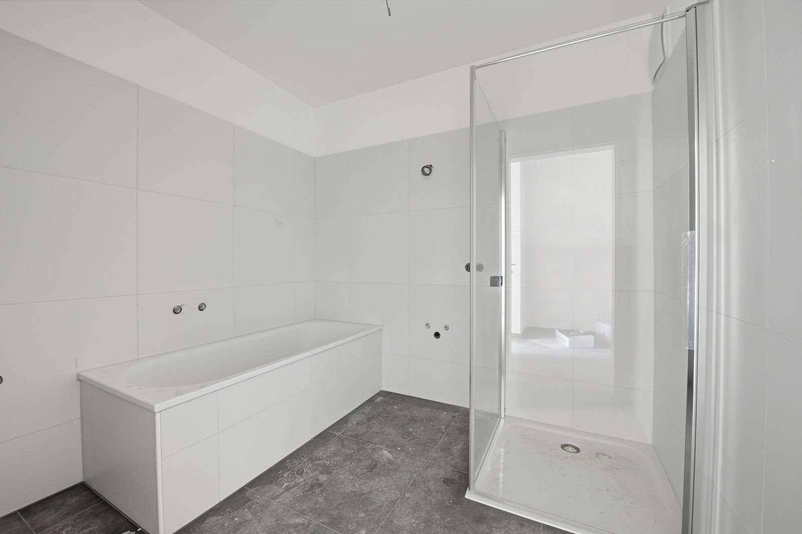 Unmöbliertes Badezimmer mit Badewanne und Duschkabine, bereit für die Fertigstellung.