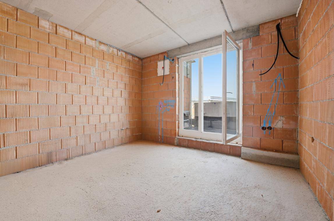Leerer Raum im Rohbau mit Ziegelwänden, Betonboden und Zugang zu einem Außenbereich.