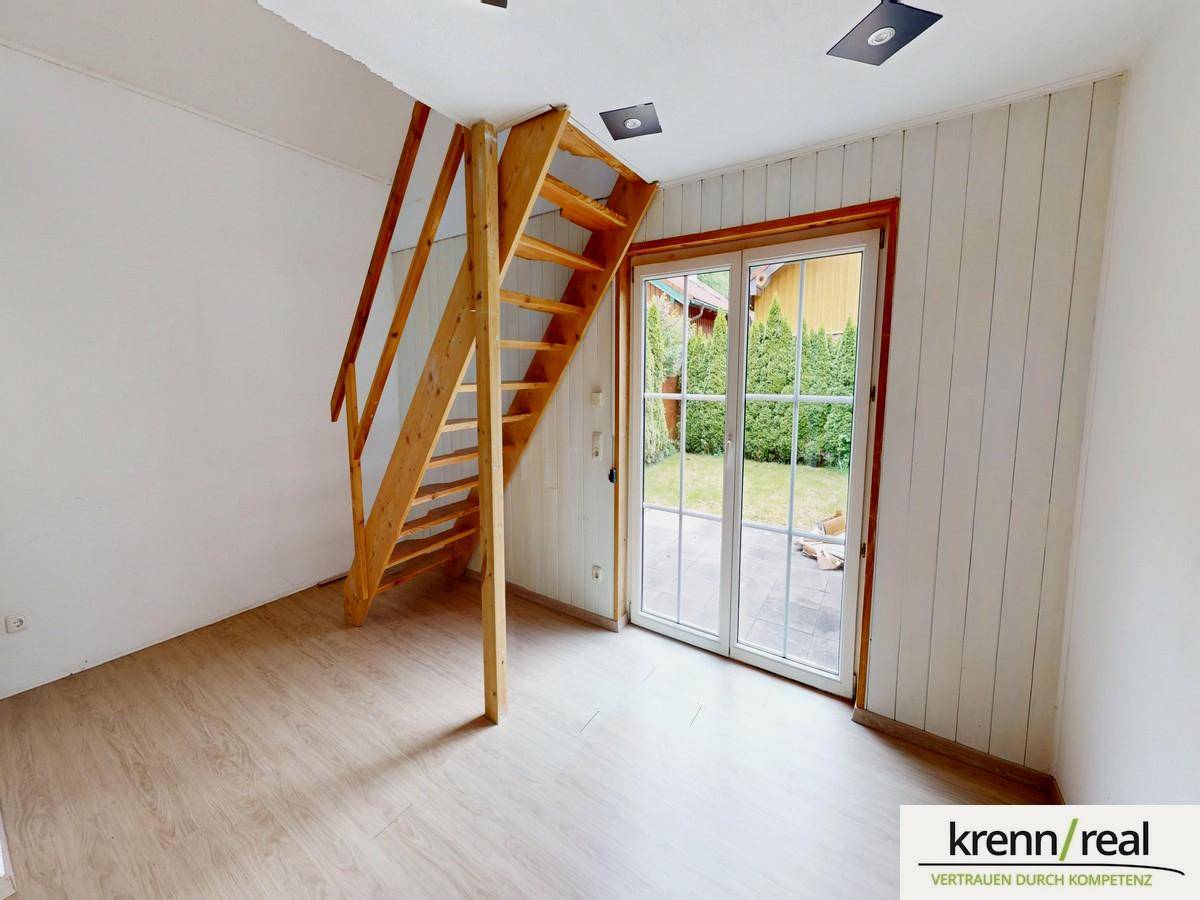 Heller Raum mit Holztreppe, Laminatboden und großer Glasschiebetür zum Gartenbereich.