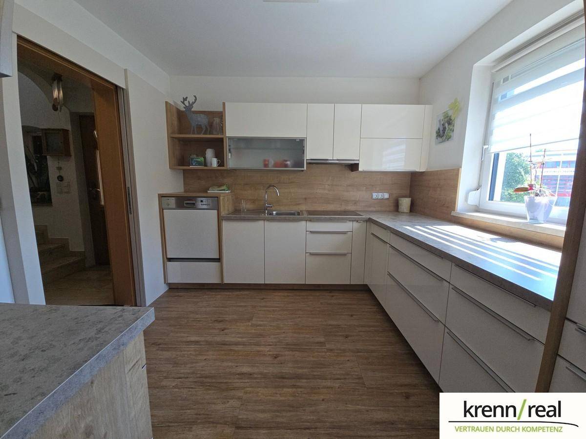 Helle Küche mit modernen weißen Schränken, Holzoptik-Arbeitsplatte und Fenster mit Ausblick.