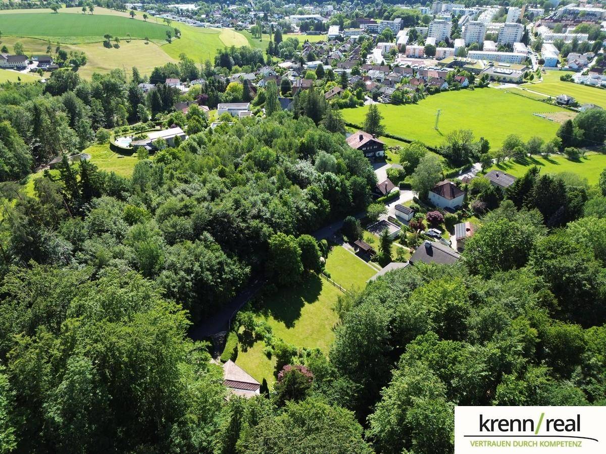 Weitläufige Luftaufnahme eines Anwesens eingebettet in grüne Natur mit Stadt im Hintergrund.