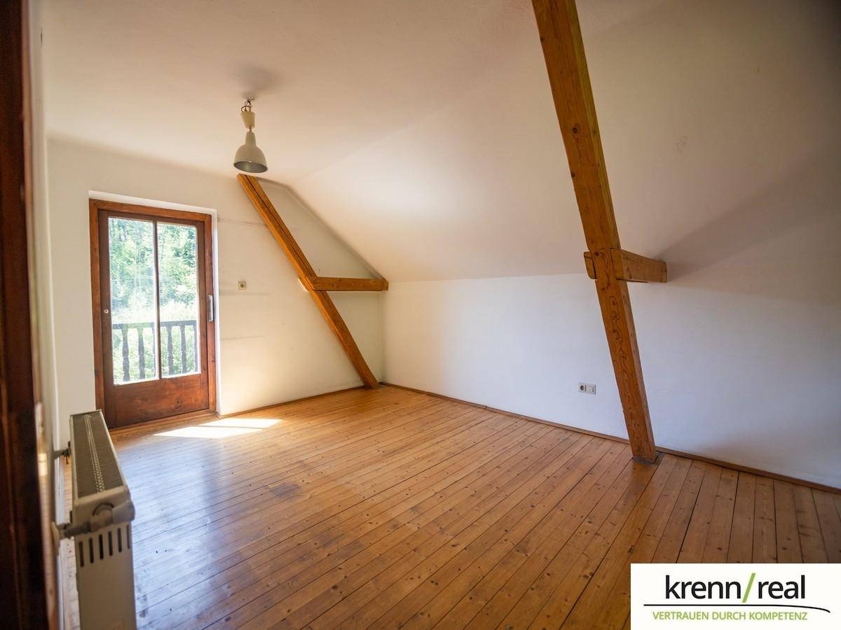 Geräumiges Schlafzimmer im Dachgeschoss mit Holzboden, sichtbaren Balken und viel Tageslicht.