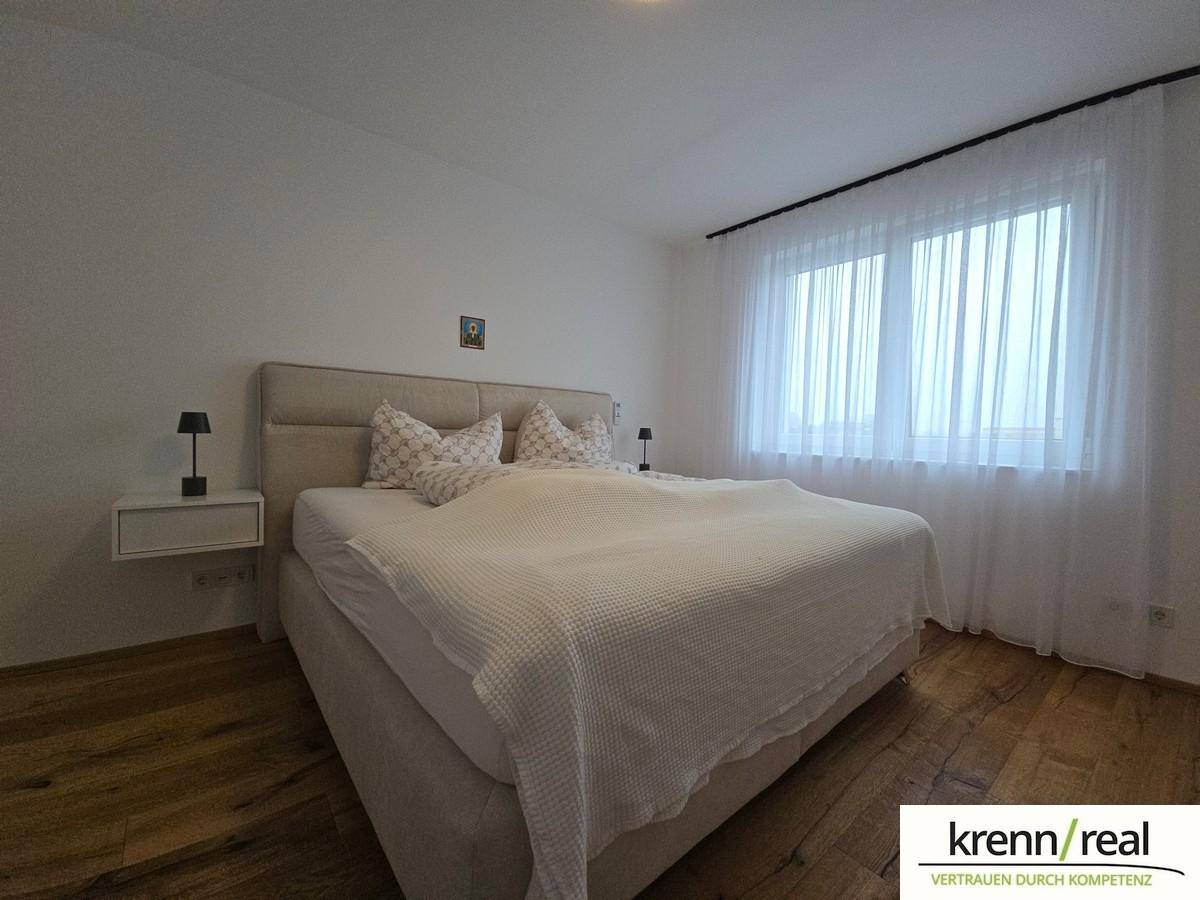 Helles Schlafzimmer mit Doppelbett, Holzboden und großen Fenstern.