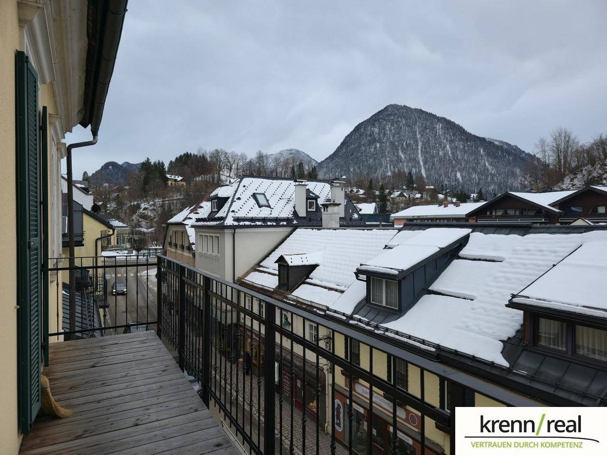 Balkon mit Holzboden und Blick auf schneebedeckte Dächer und Berge.