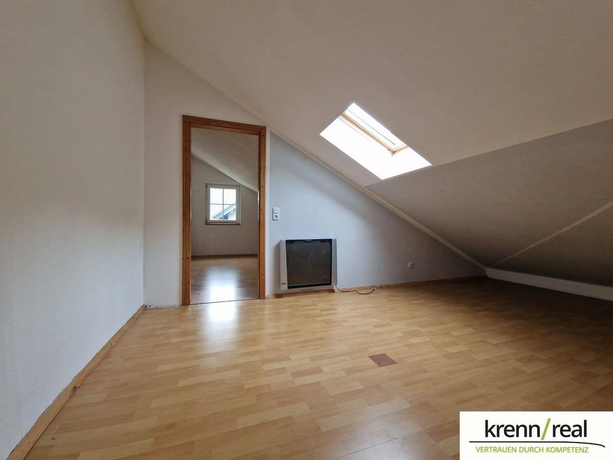 Gemütliches Dachgeschosszimmer mit schrägen Wänden, Laminatboden und einem Dachfenster für natürliches Licht.