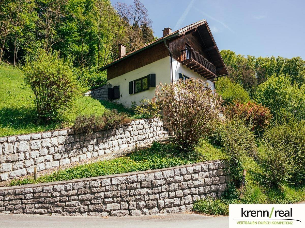 Haus in Hanglage mit rustikalen Steinmauern und grüner Bepflanzung in sonniger Umgebung.