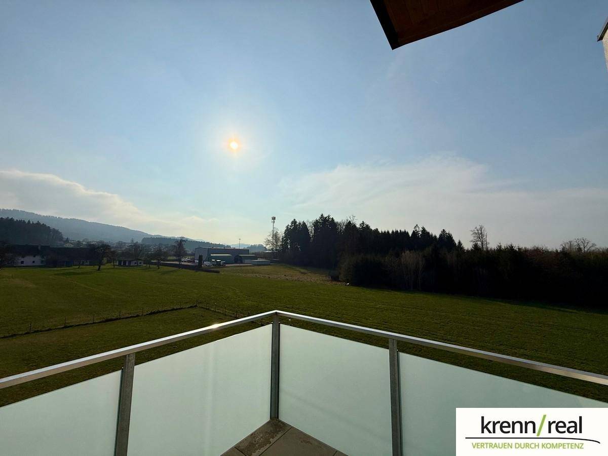Weitläufiger Blick über grüne Felder und die umliegende Landschaft von einem sonnigen Balkon.