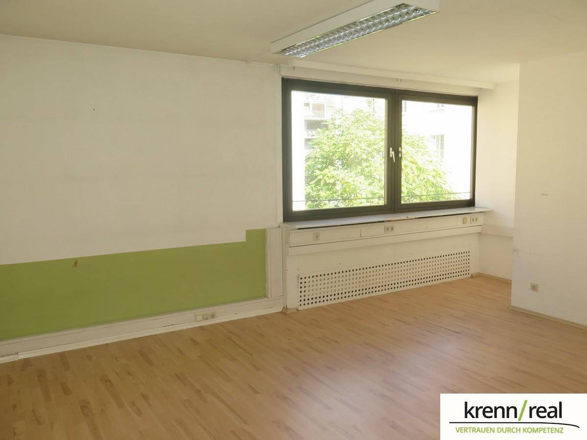 Büro mit Laminatboden, großen Fenstern und einer grünen Akzentwand, bietet einen Blick ins Grüne.