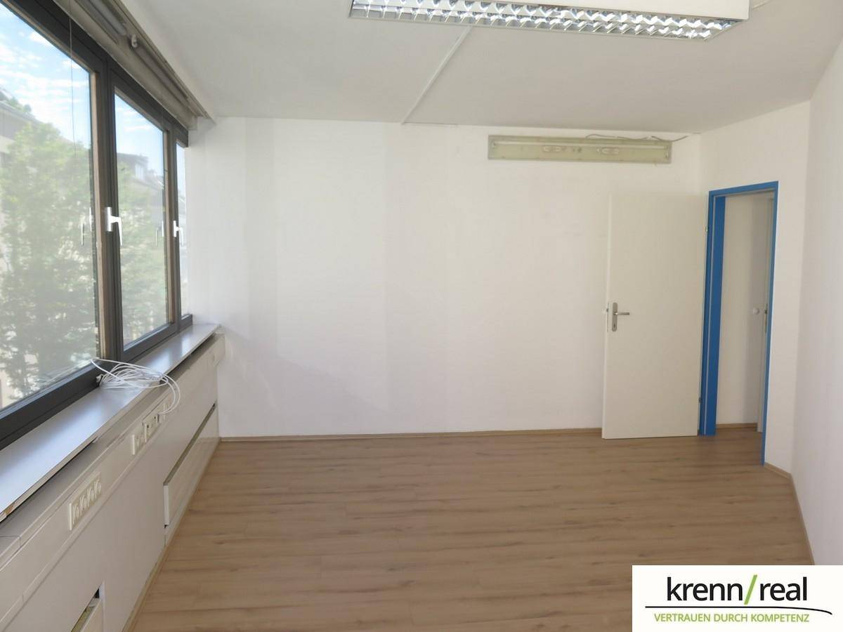 Büro mit Laminatboden, großen Fenstern und einer Tür mit blauem Rahmen, bereit zur individuellen Gestaltung.