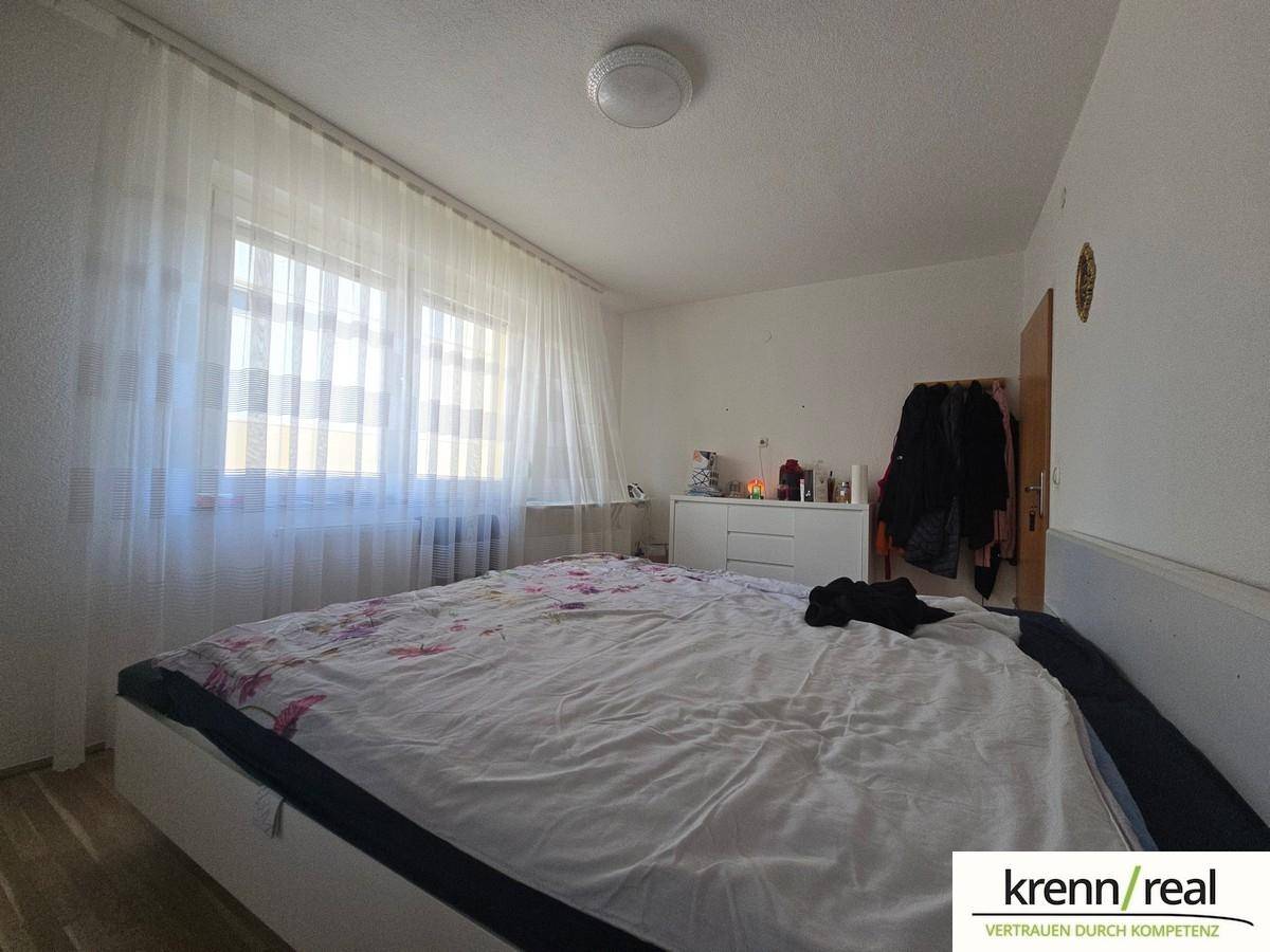 Helles Schlafzimmer mit großem Doppelbett, weißer Kommode und viel Tageslicht durch das Fenster.