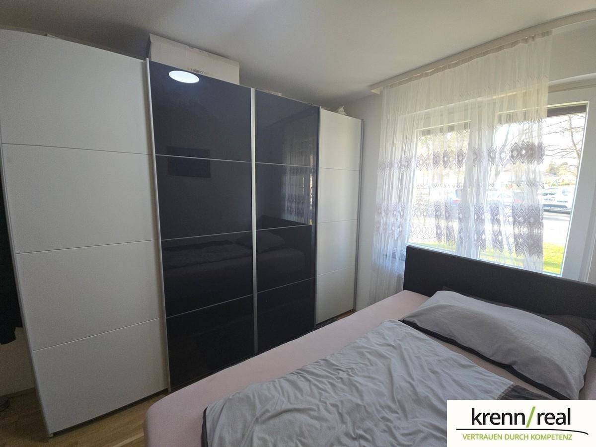 Schlafzimmer mit modernem Kleiderschrank in Weiß und Schwarz sowie einem Fenster mit Vorhängen.