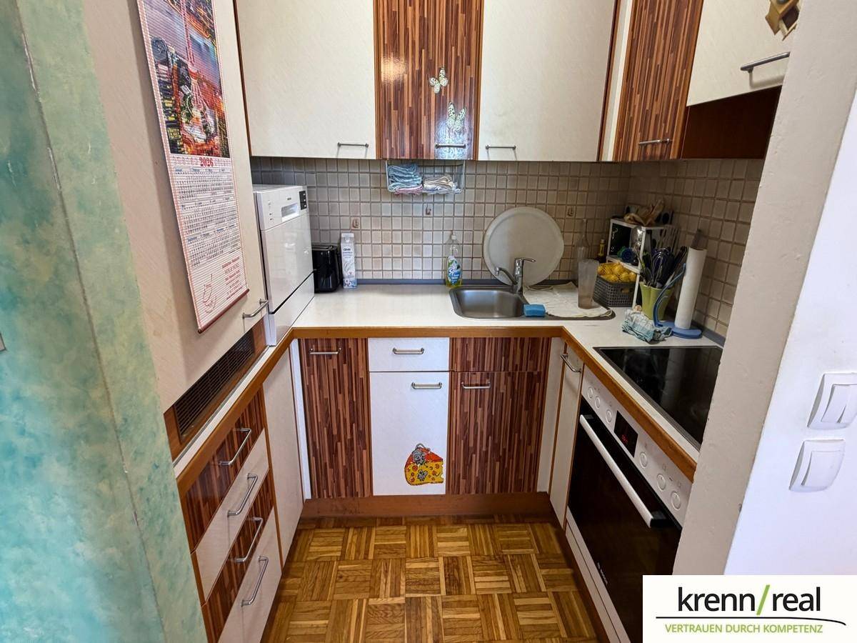 Funktionale Küche mit älteren Holzfronten, Fliesenrückwand und integrierten Geräten.