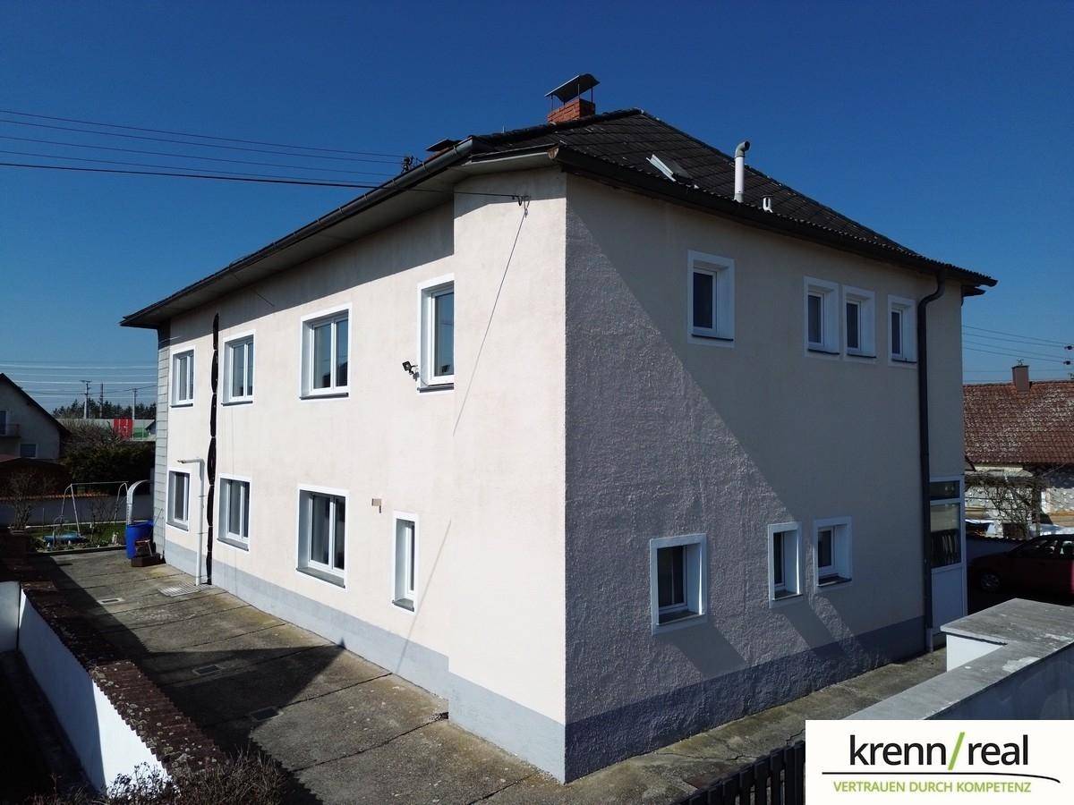 Seitenansicht des Wohnhauses mit hellbeiger Fassade und weißen Fenstern unter blauem Himmel.