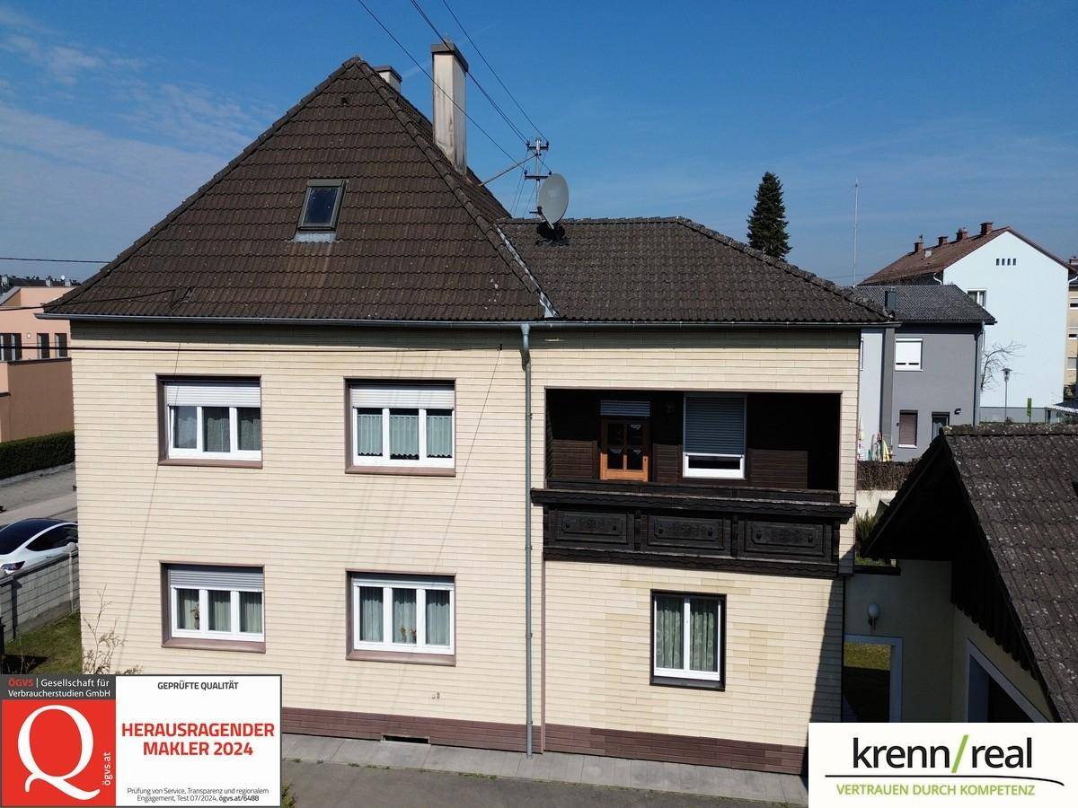 Vorderansicht eines Wohnhauses mit Satteldach und mehreren Fenstern unter blauem Himmel.